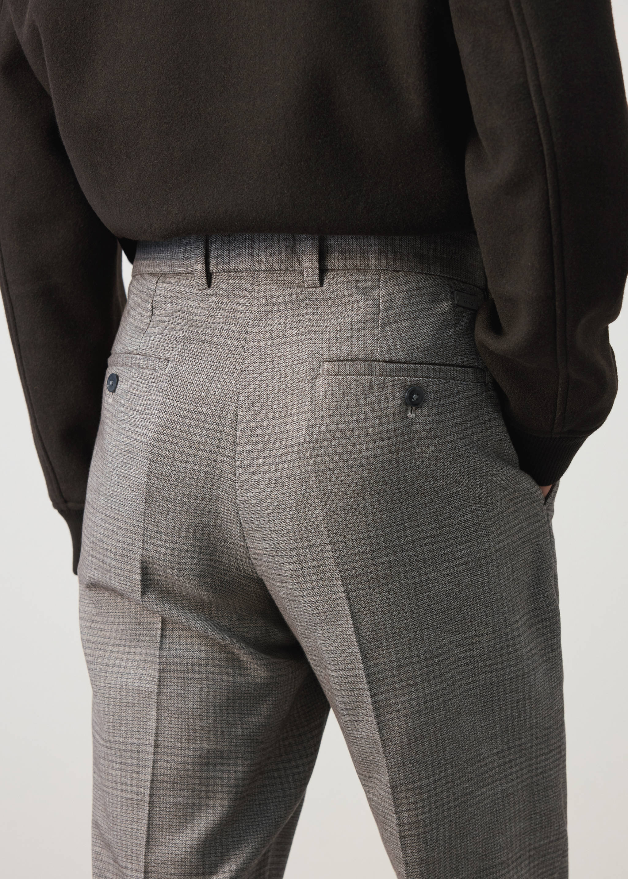 Grey houndstooth trousers with rear buttoned pockets, seen from behind.