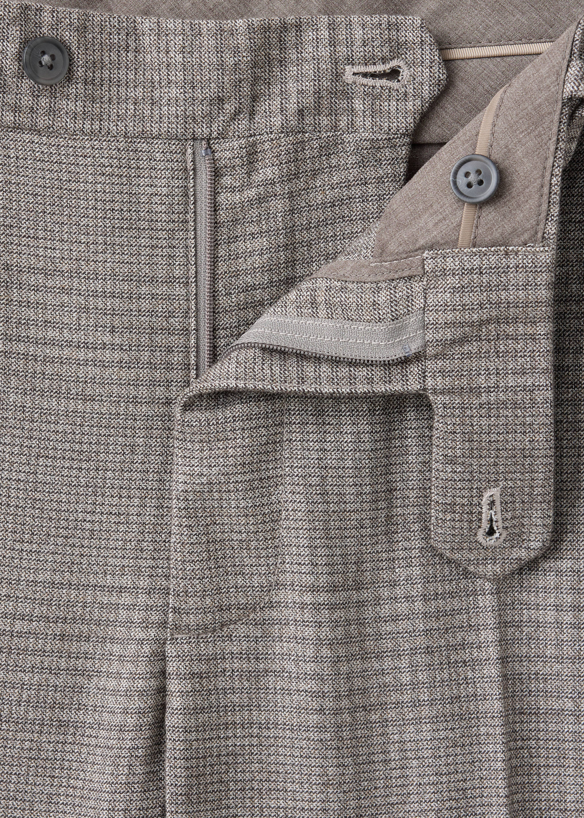 Close-up of the waistband and zip fly on brown patterned trousers.
