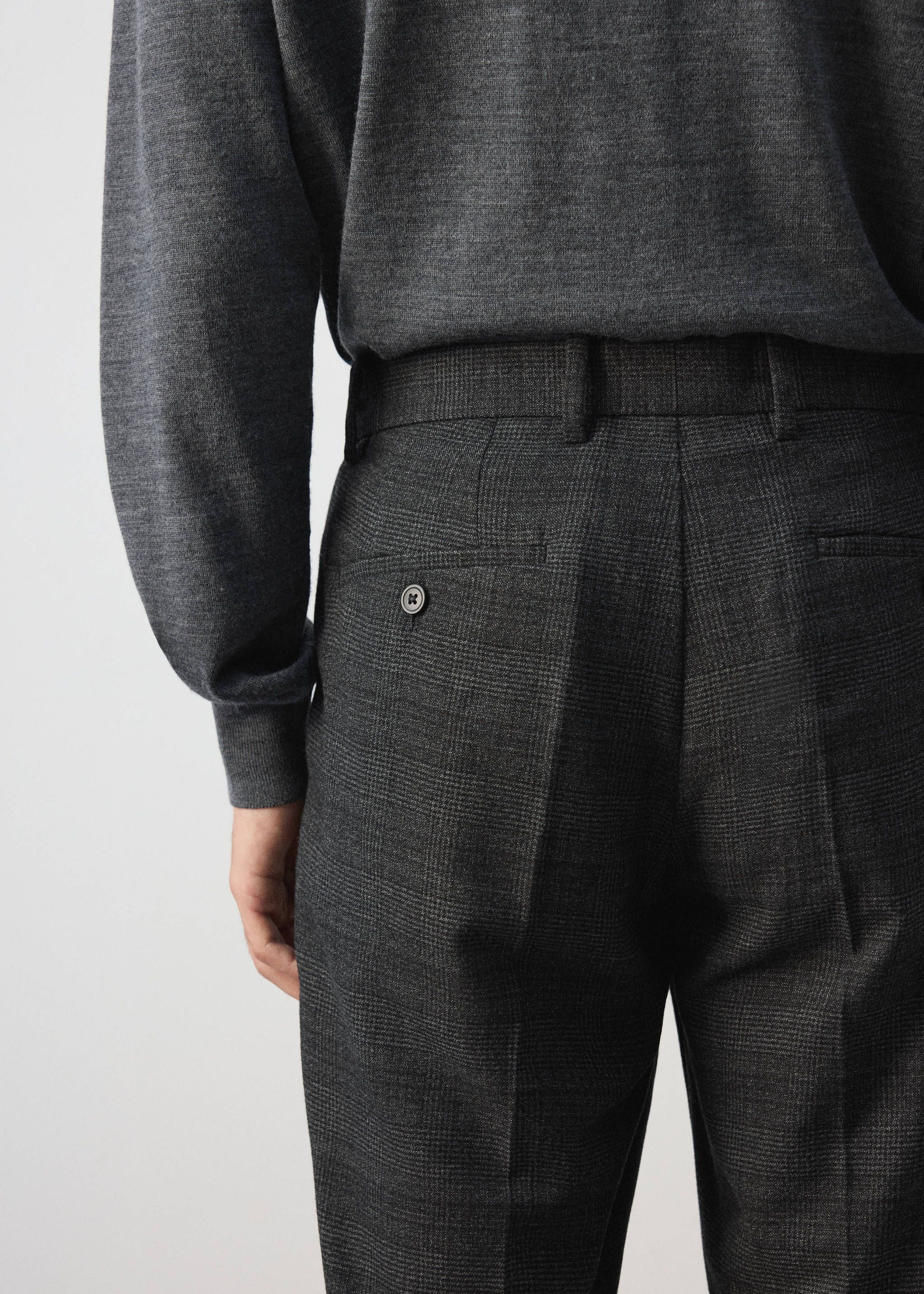 Dark grey plaid trousers with belt loops and a back button pocket, back view.