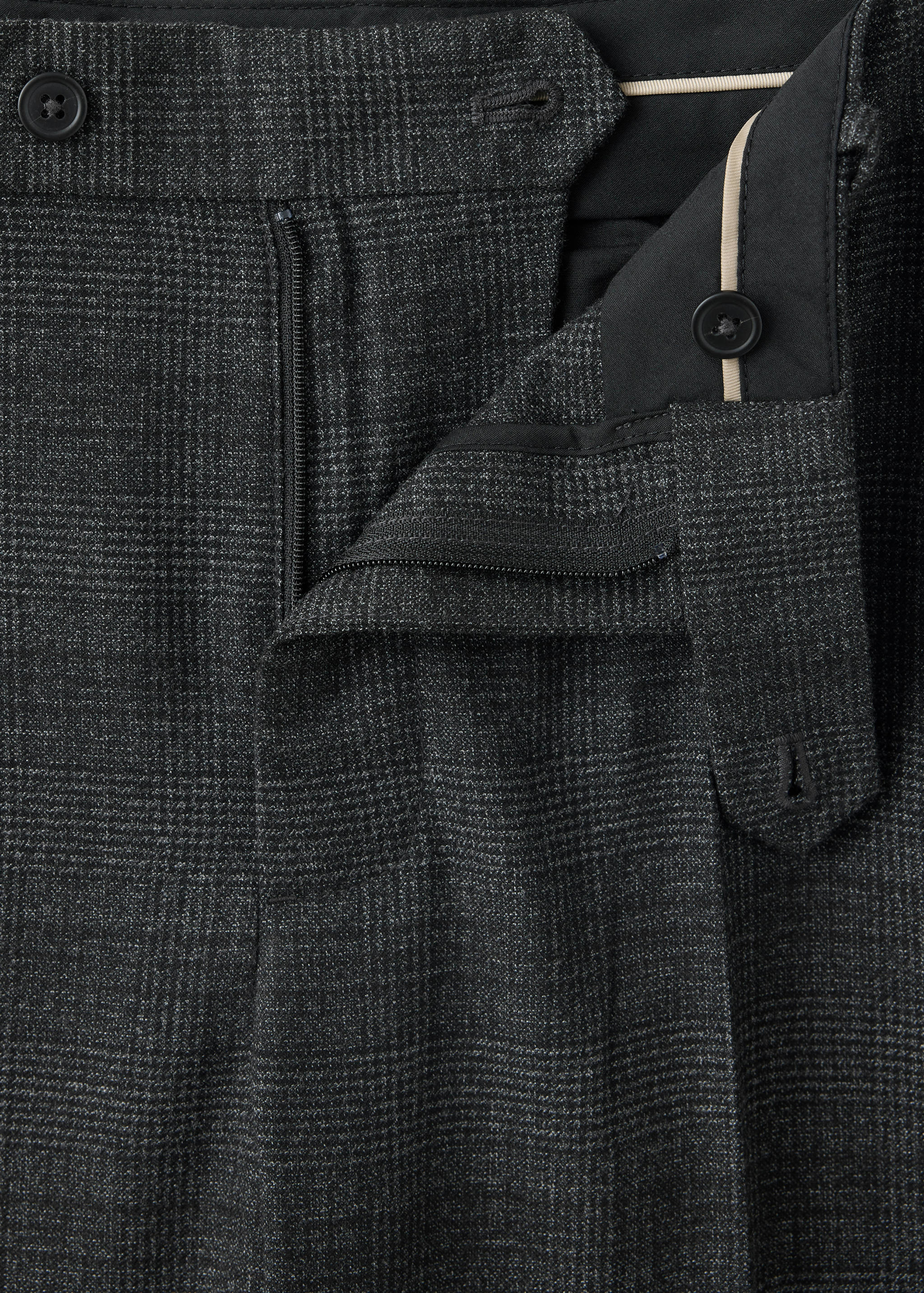 Close-up of the waistband and fastening on dark grey checked trousers.