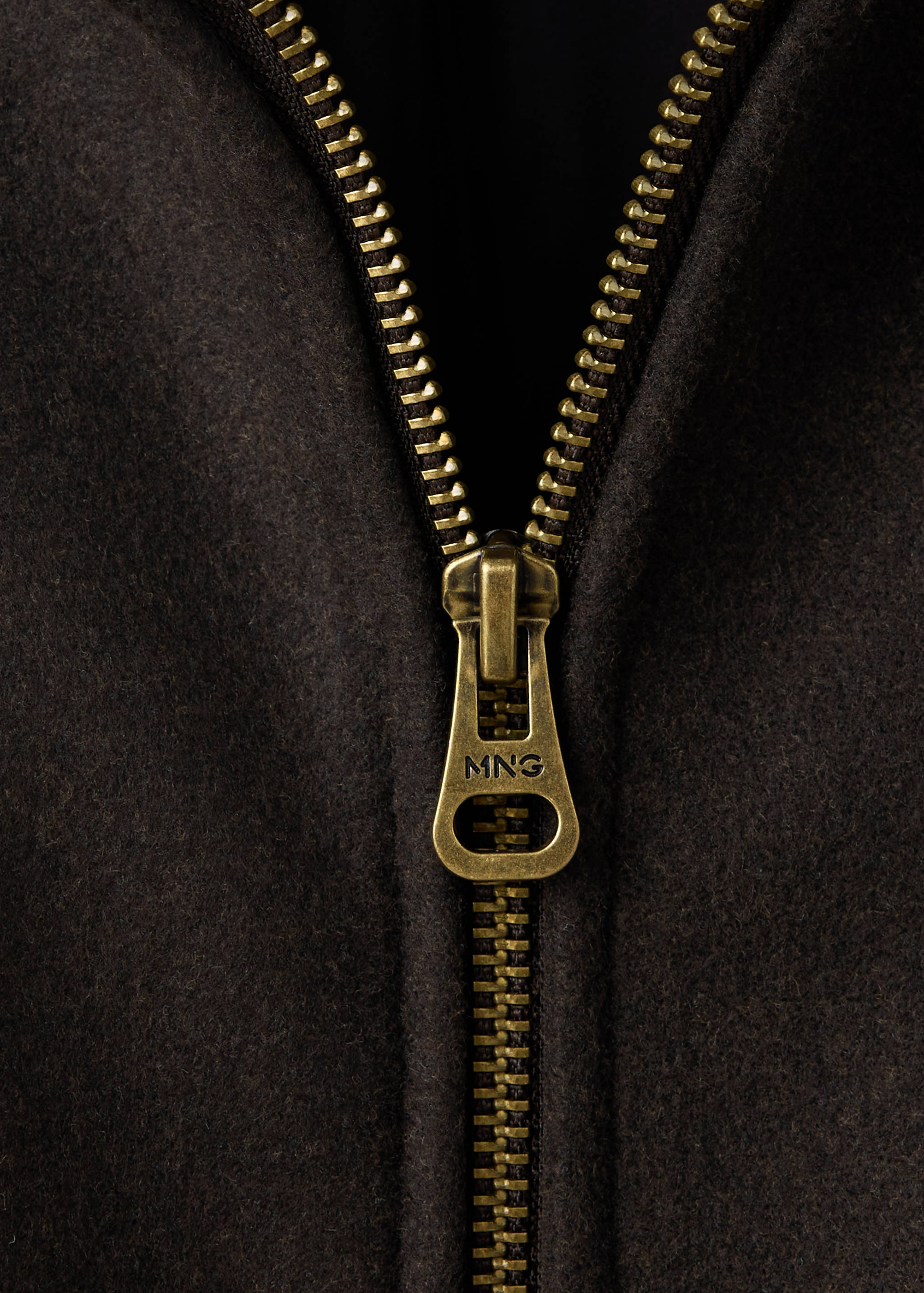 Close-up of a dark brown jacket featuring an antique brass zipper.