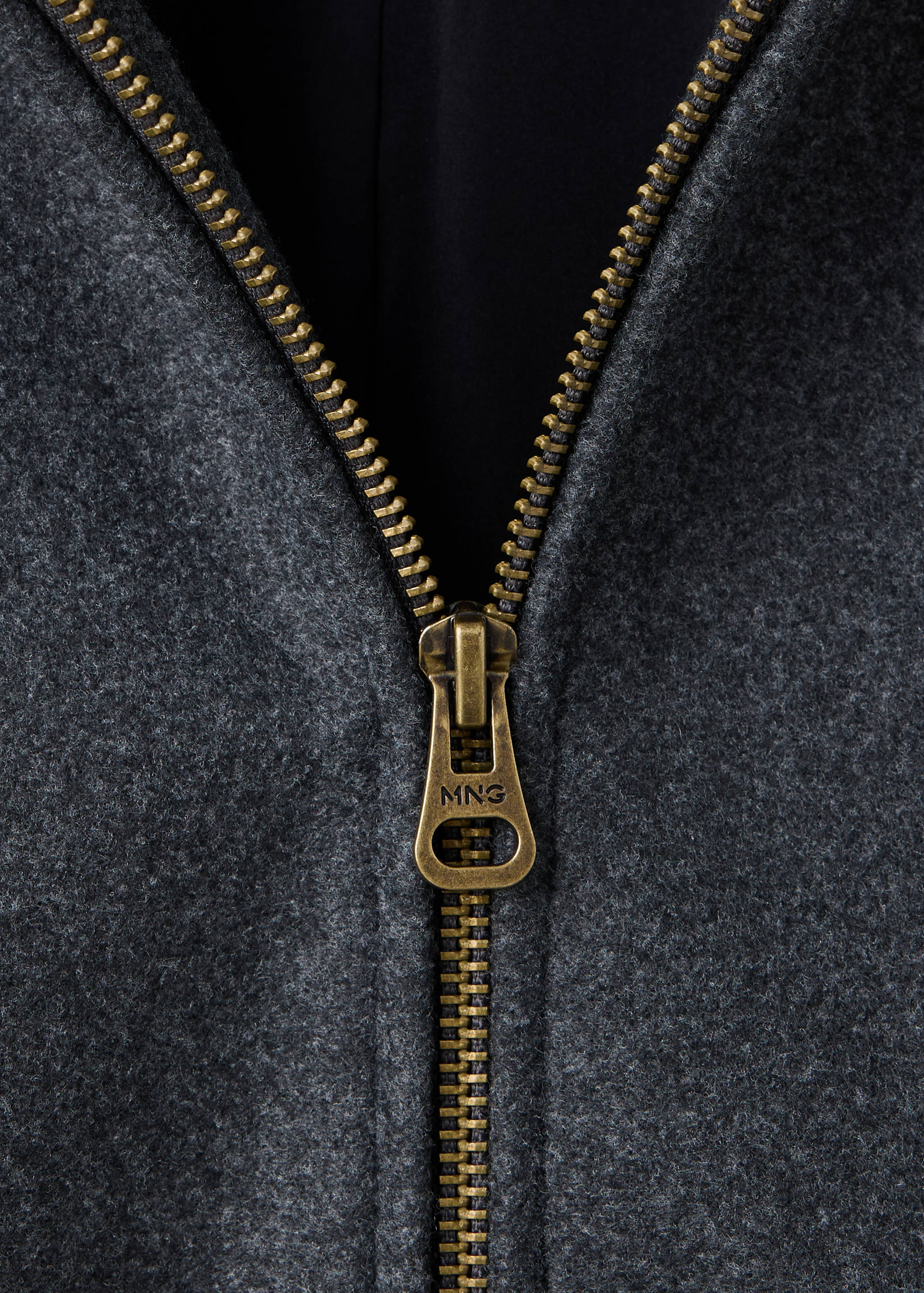 Close-up of a grey jacket showing the antique brass zipper detail.