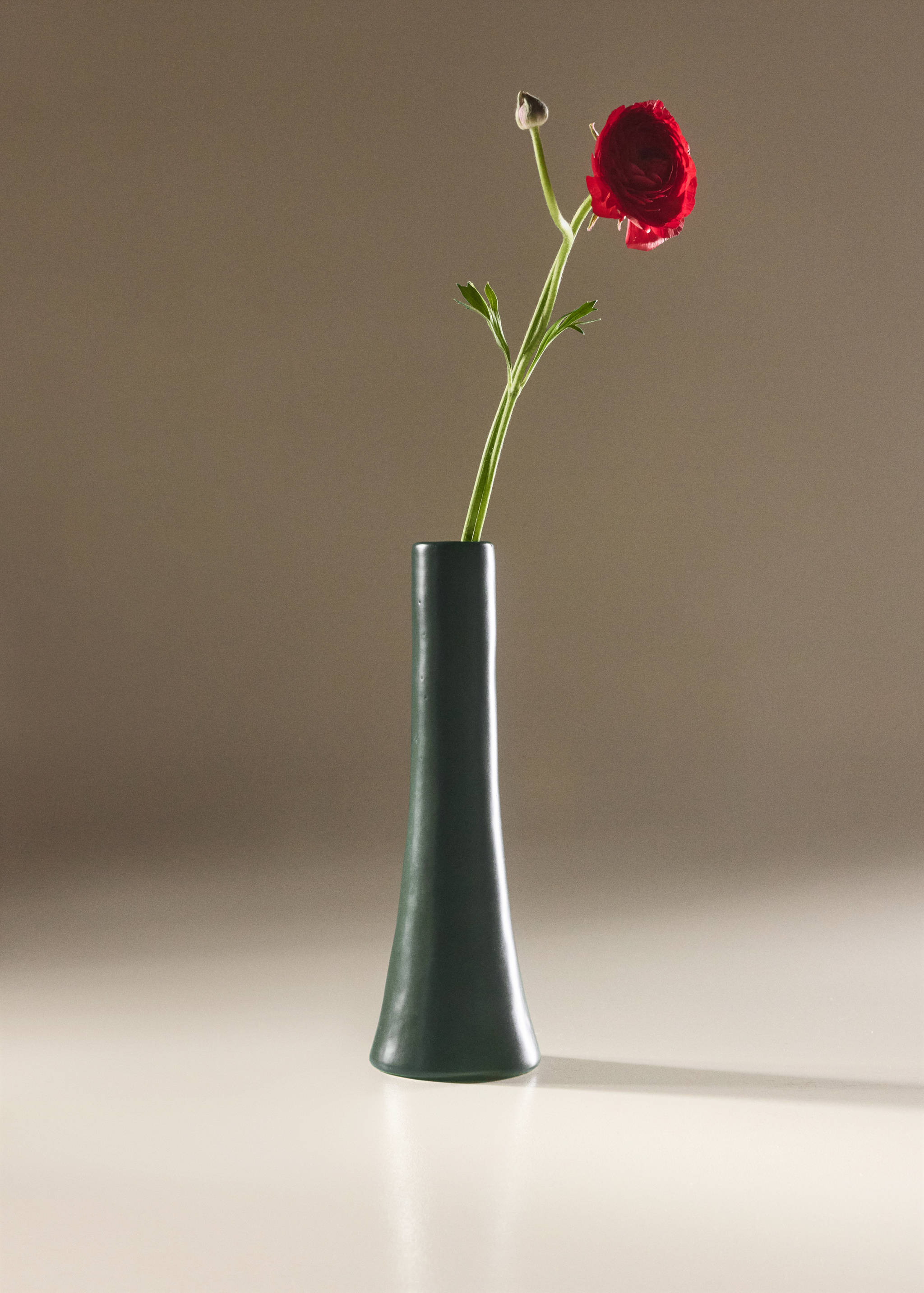 Dark green cylindrical candle holder holding a red flower.