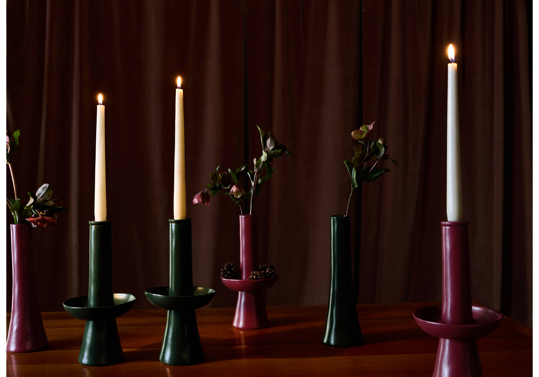 Dark green and burgundy ceramic candleholders arranged with lit white candles and vases.