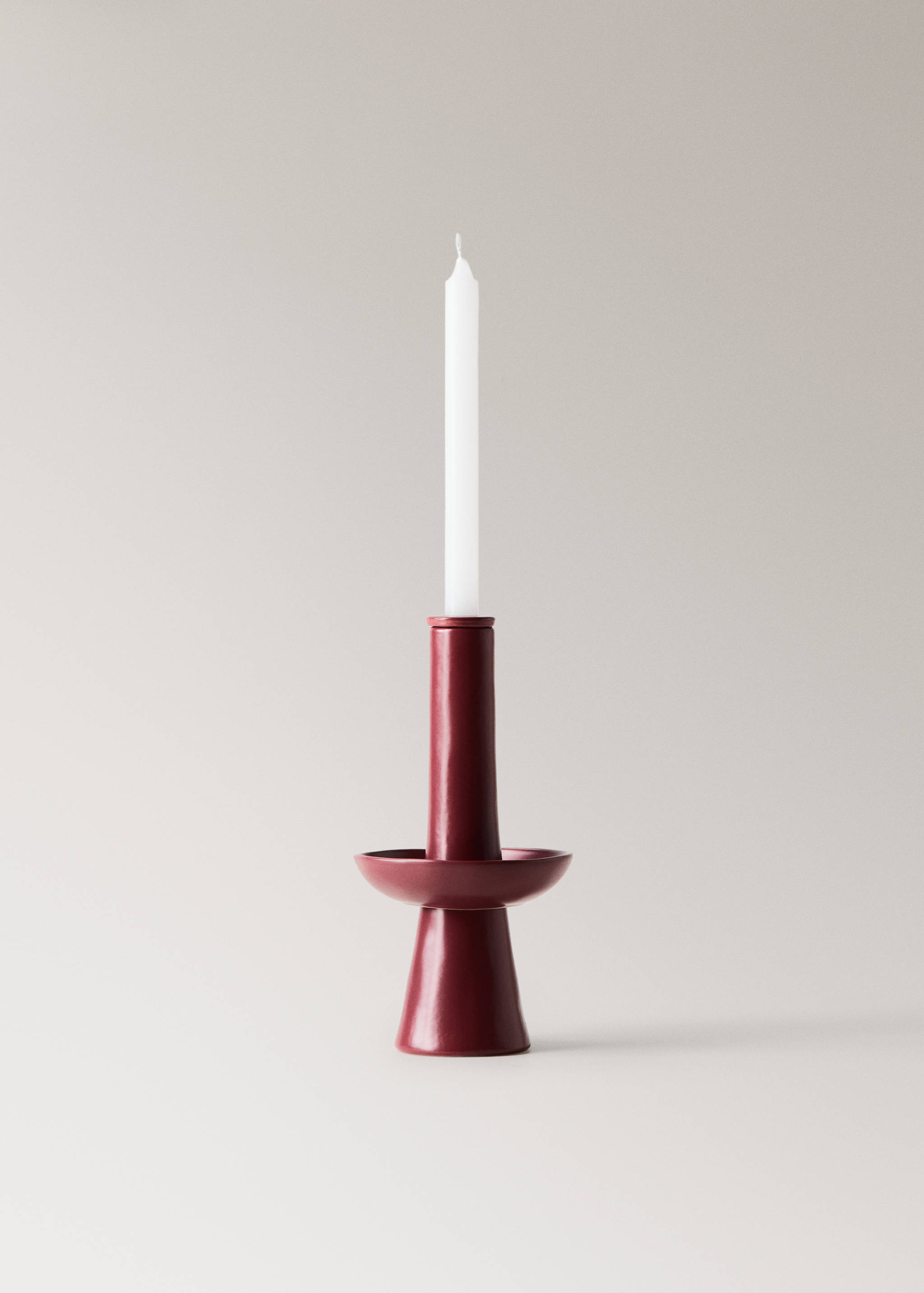 Dark red ceramic candle holder with a flared base and white taper candle.