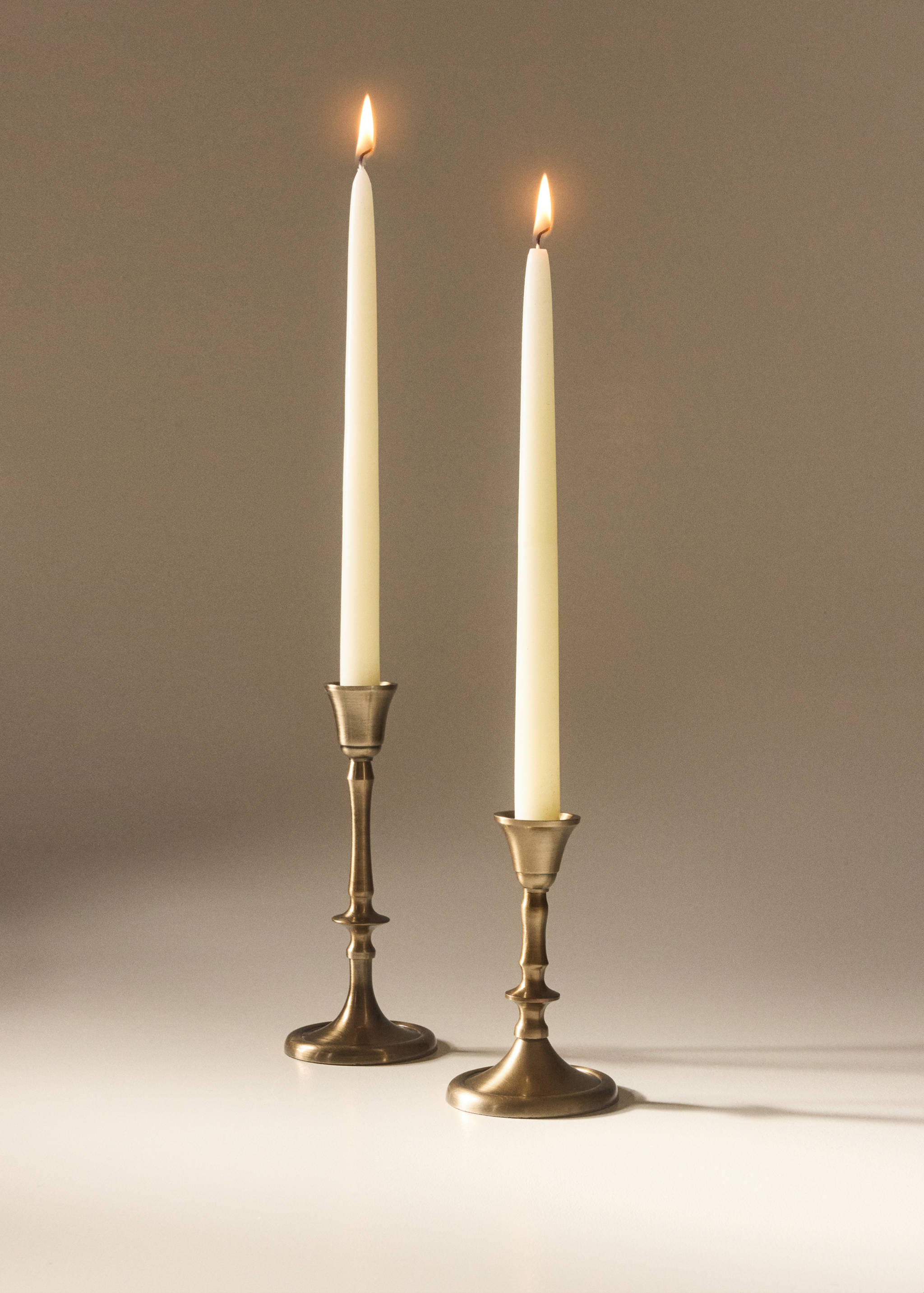 Two antique bronze candlestick holders with lit white taper candles.