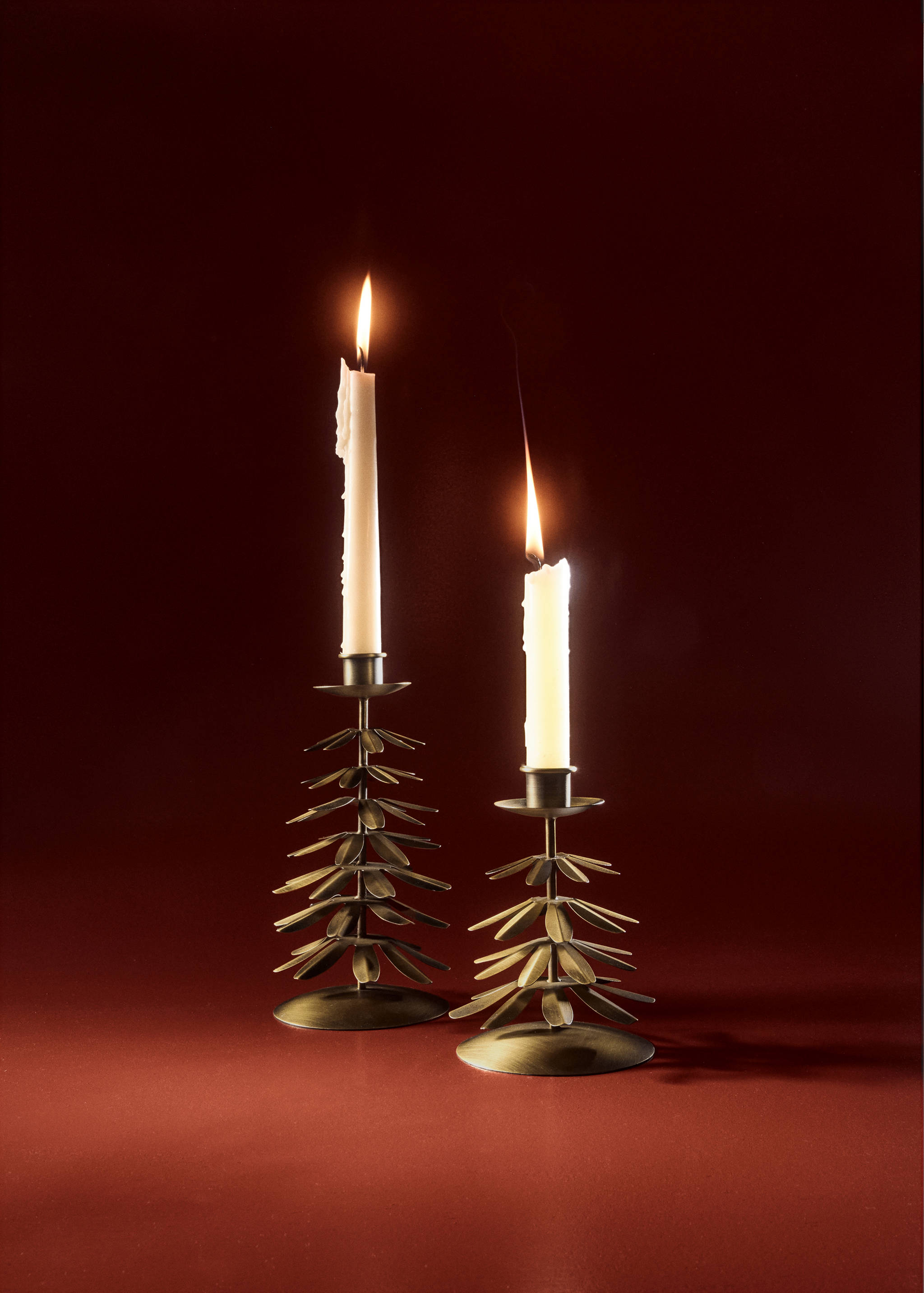 Two brass-toned metal tree-shaped candle holders with lit white candles.