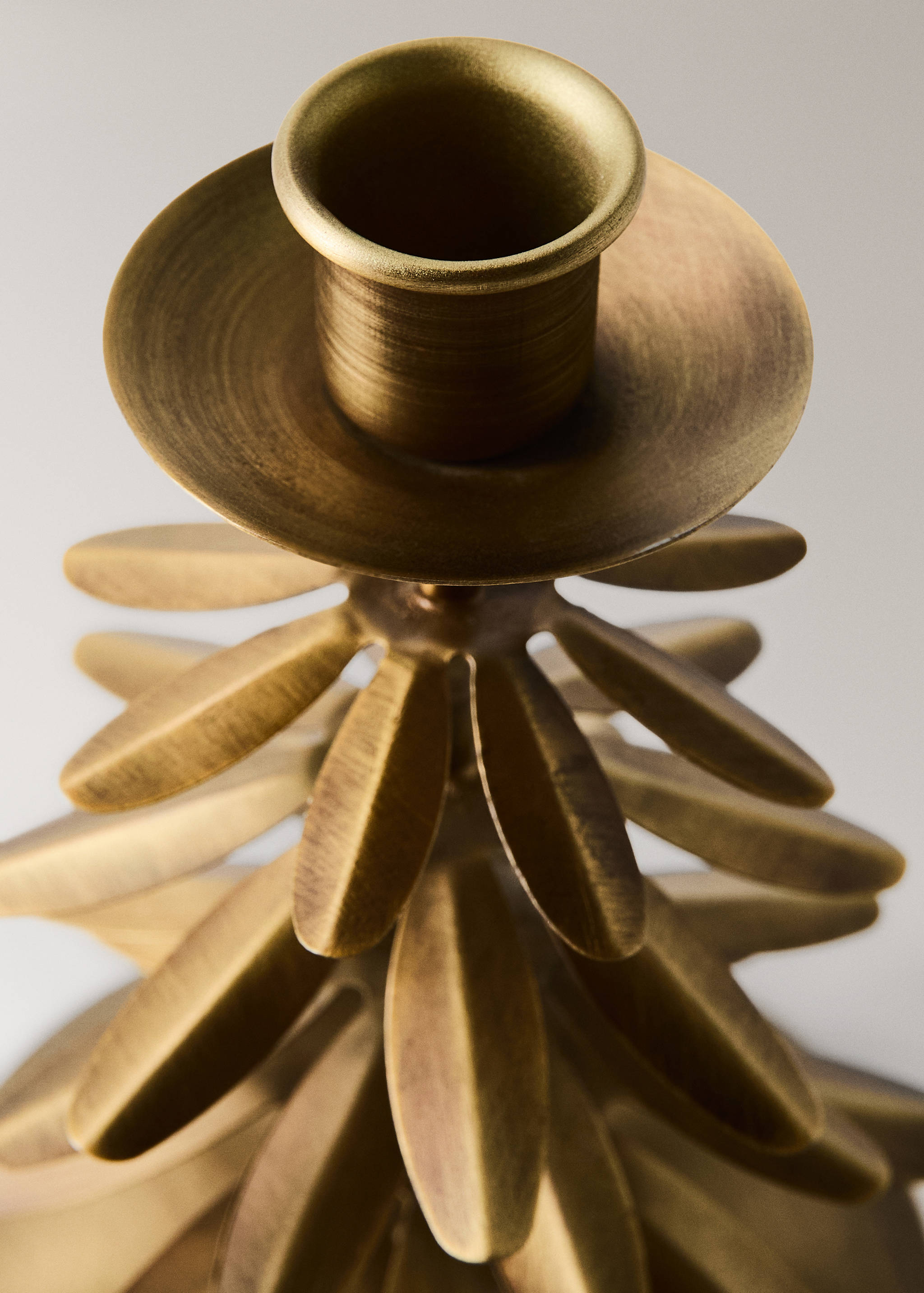 Brushed gold candle holder with a textured leaf-shaped design detail.