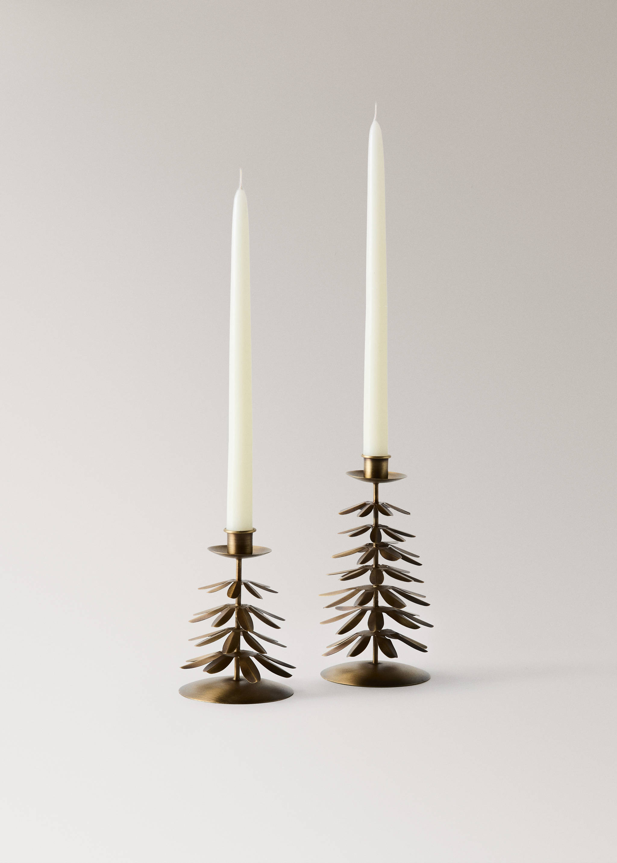 Two brass finish leaf shaped metal candle holders with white candles.