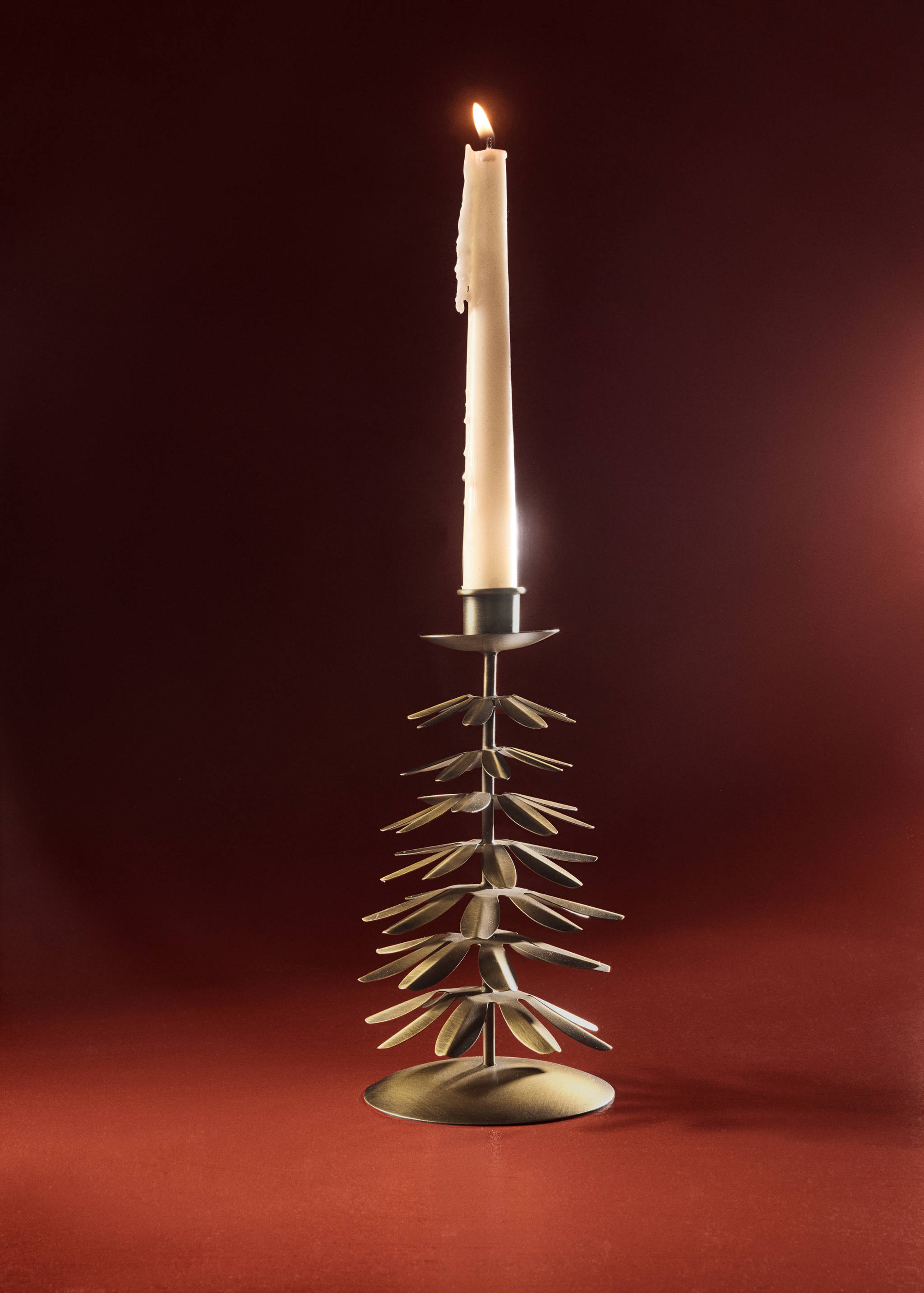 Portavelas metálico de color bronce con forma de árbol de Navidad y una vela blanca encendida.