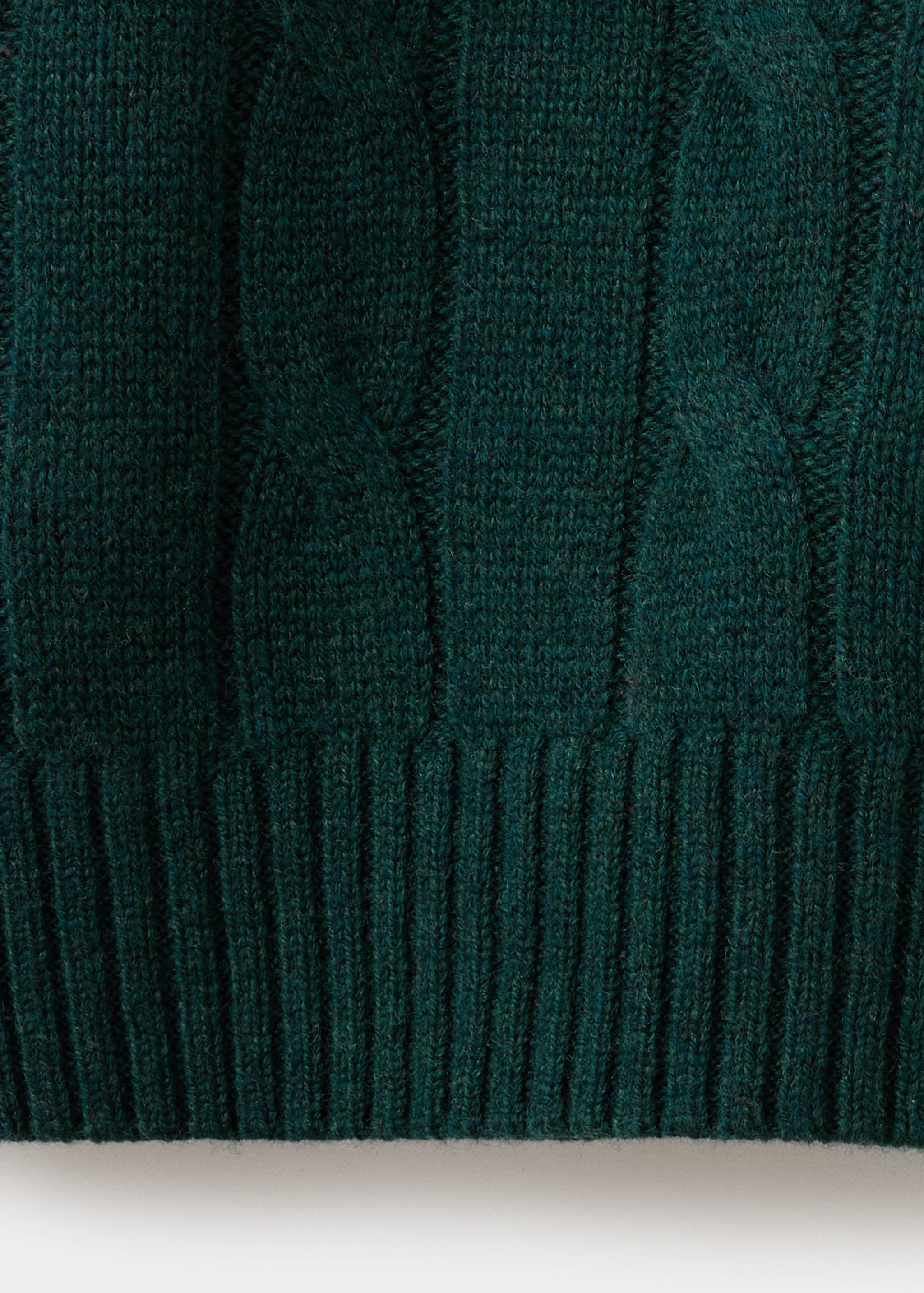 Close-up of a dark green jersey showing the cable knit texture and ribbed hem.