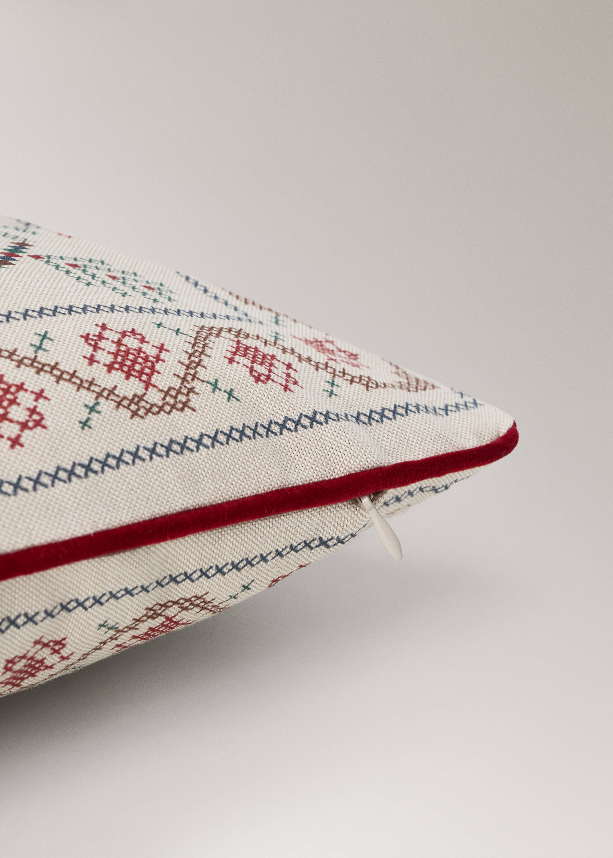 Cushion cover with a cross-stitch geometric pattern and red velvet piping.