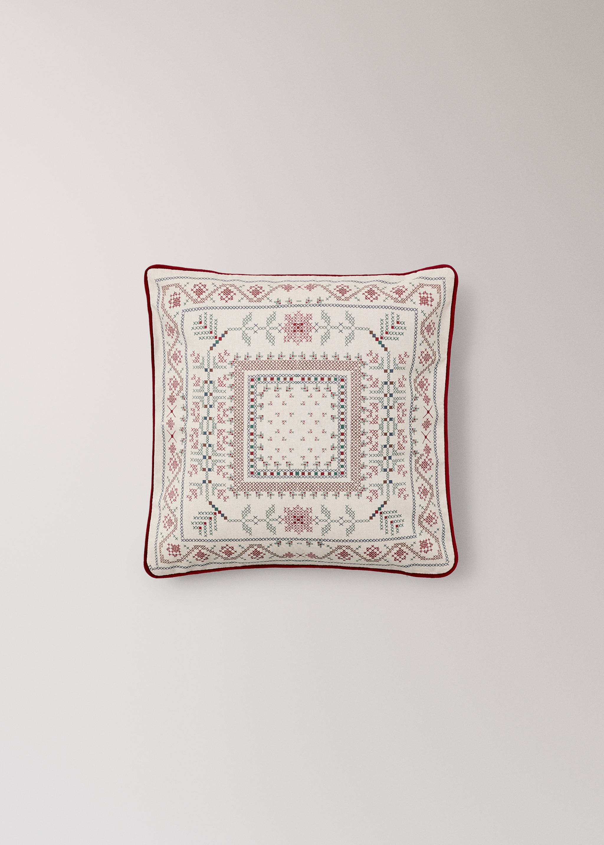 Off-white cross-stitch cushion cover with red piping.