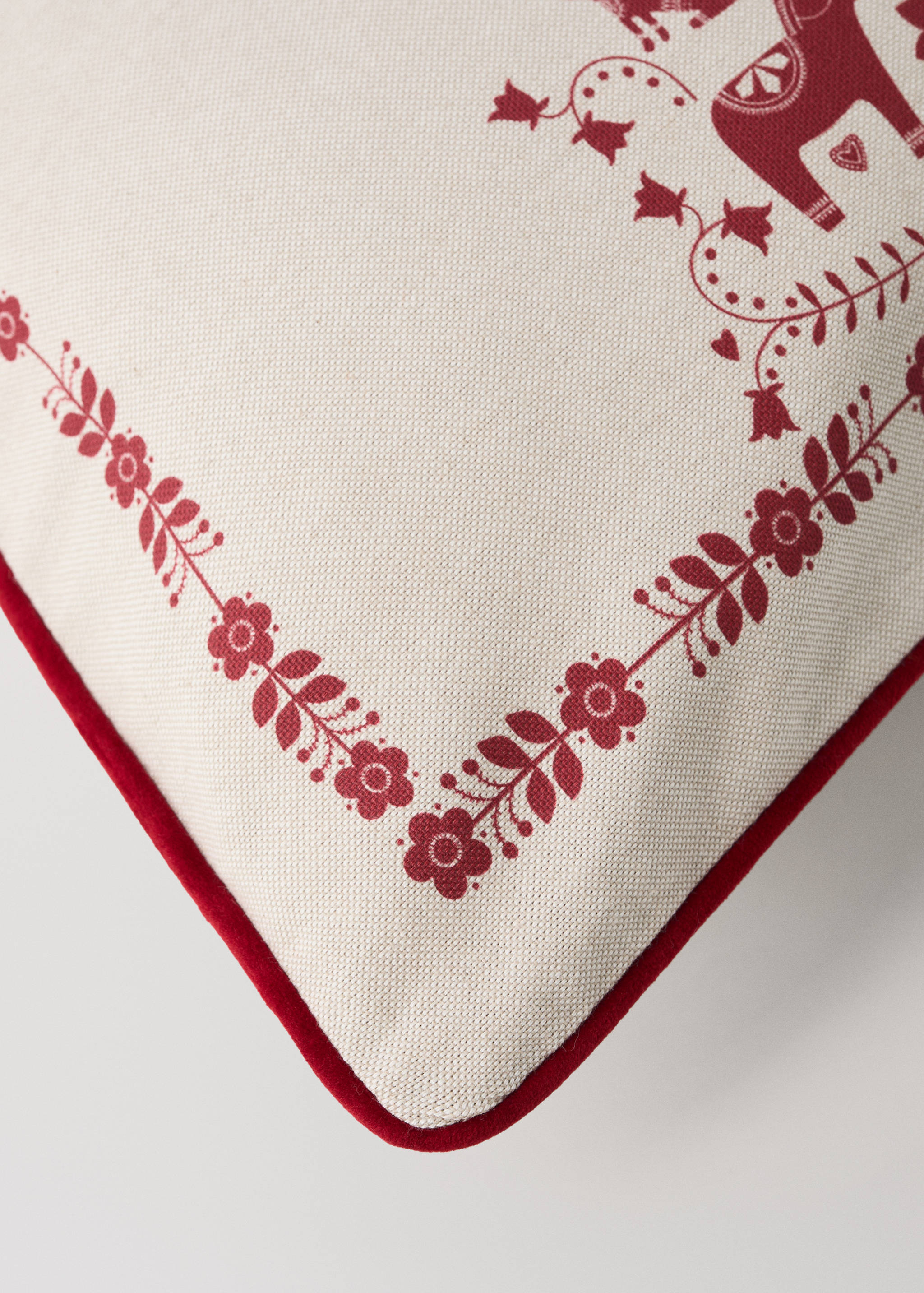 Close-up of an off-white cushion cover with red piping and a red floral folk-art border.