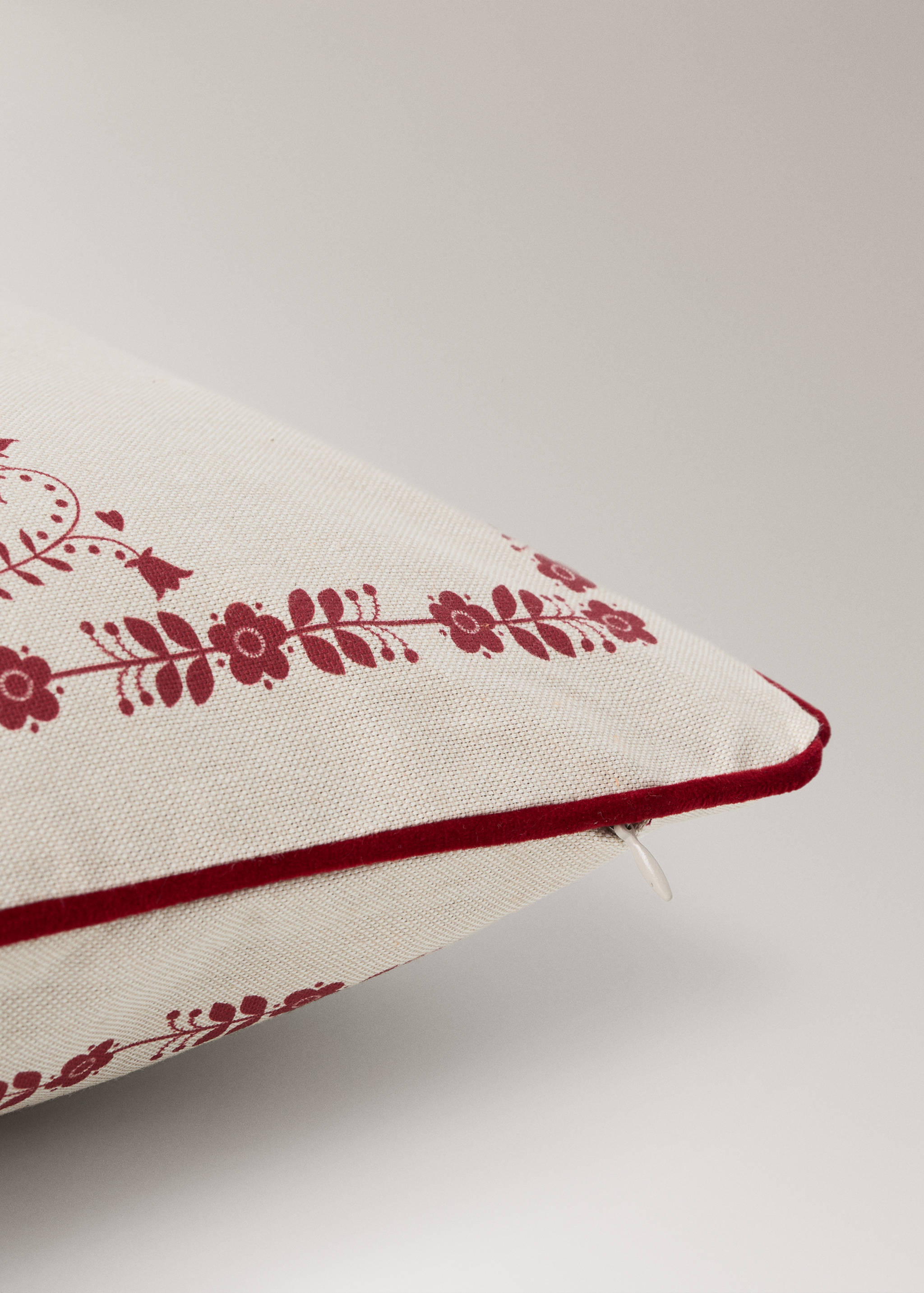 Cream cushion cover with a red floral print and velvet piping.
