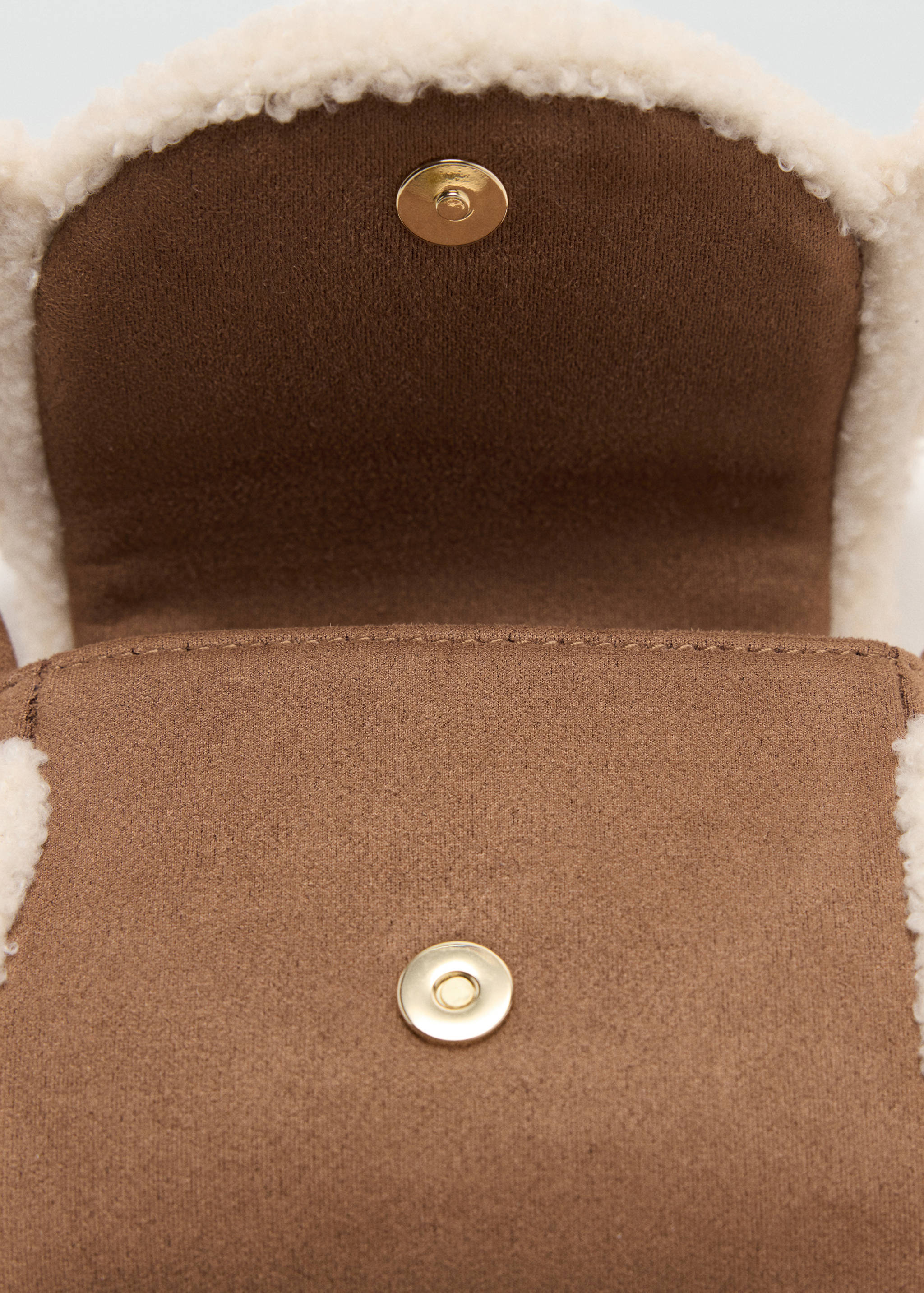 Primer plano de un minibolso marrón con ribete de borreguillo sintético en color crema y cierre magnético dorado.