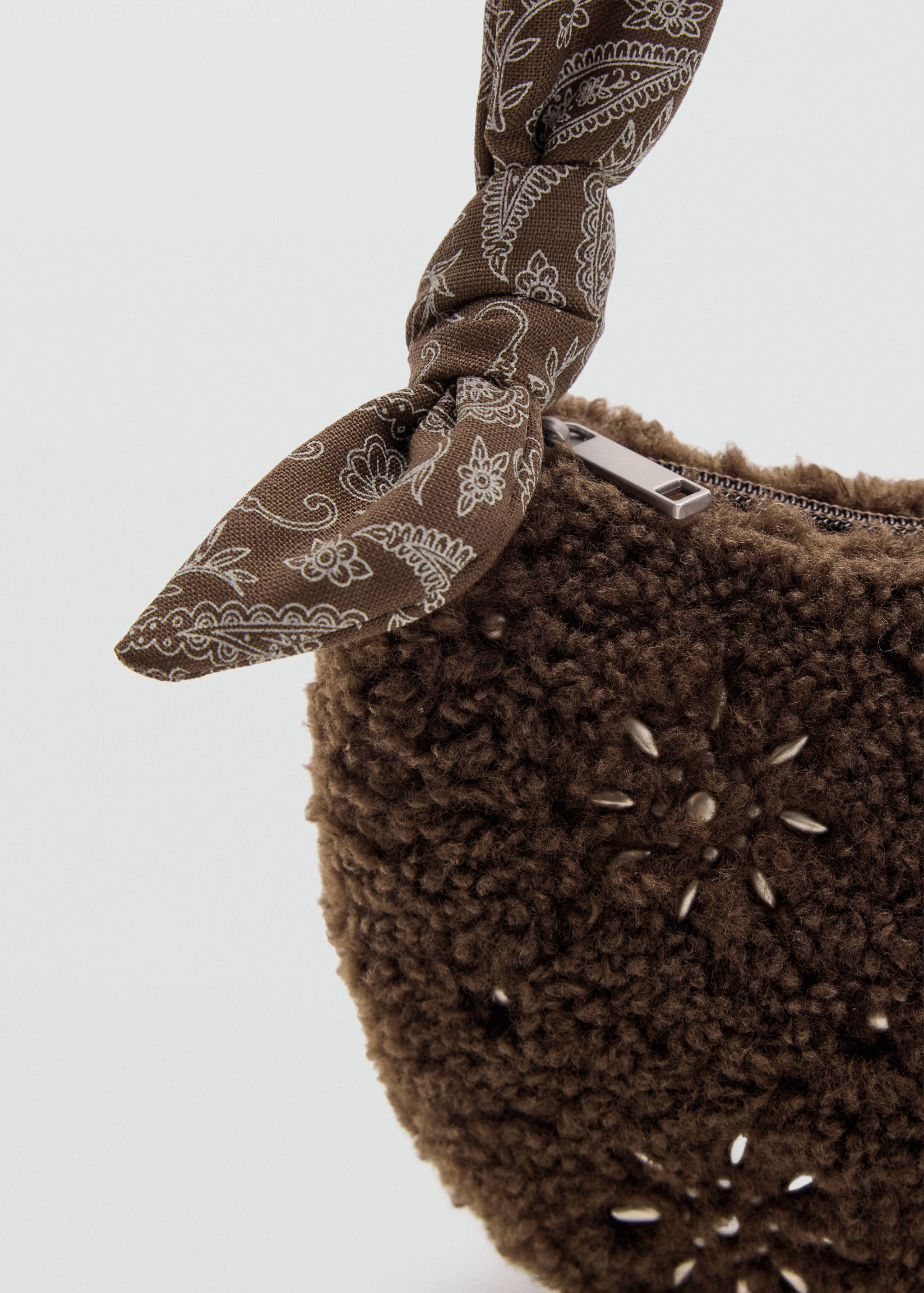 Close-up of a brown faux-fur mini bag with star studs and a knotted paisley strap.