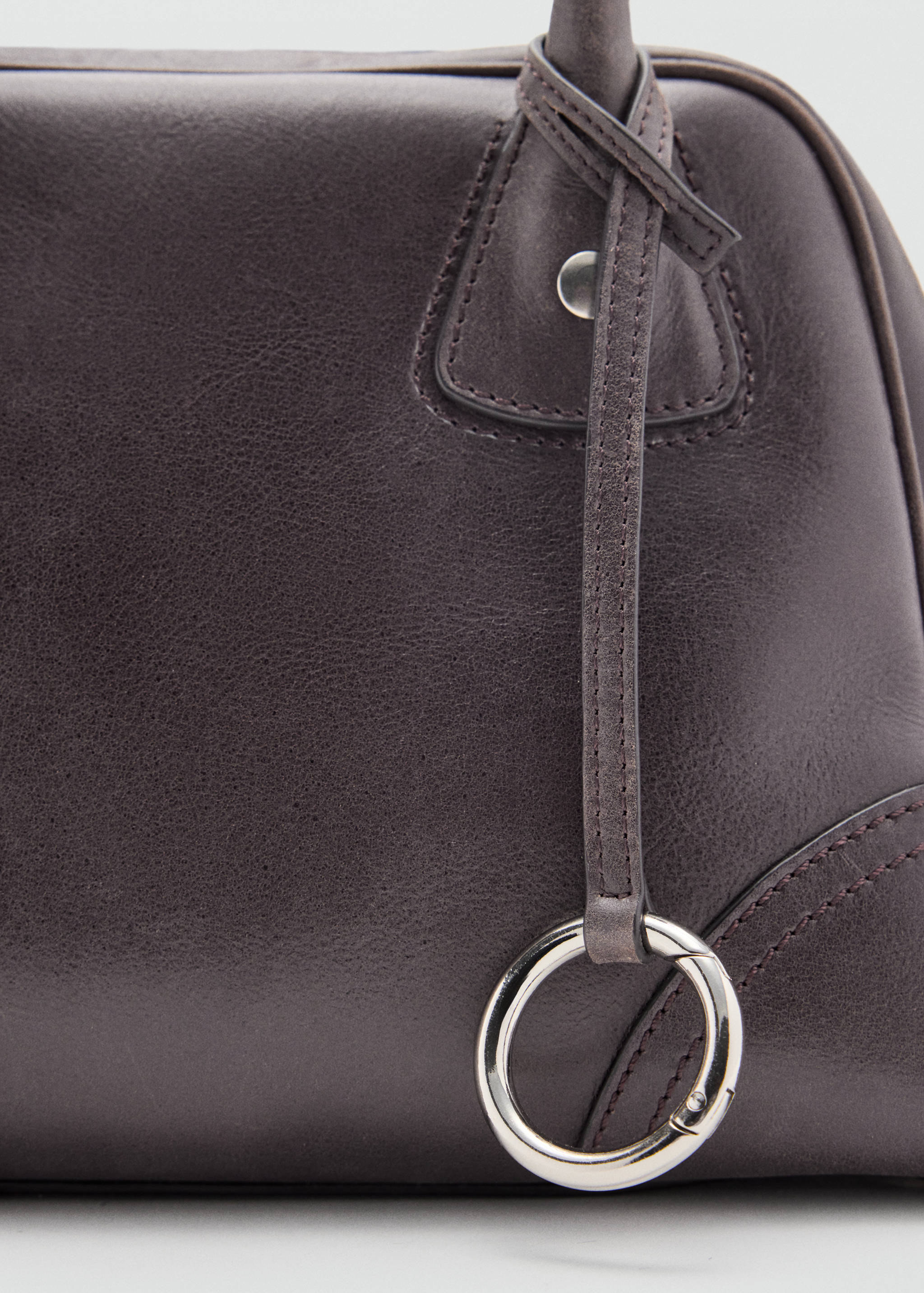 Close-up of a dark brown bowling bag showing a hanging leather strap and metal ring detail.
