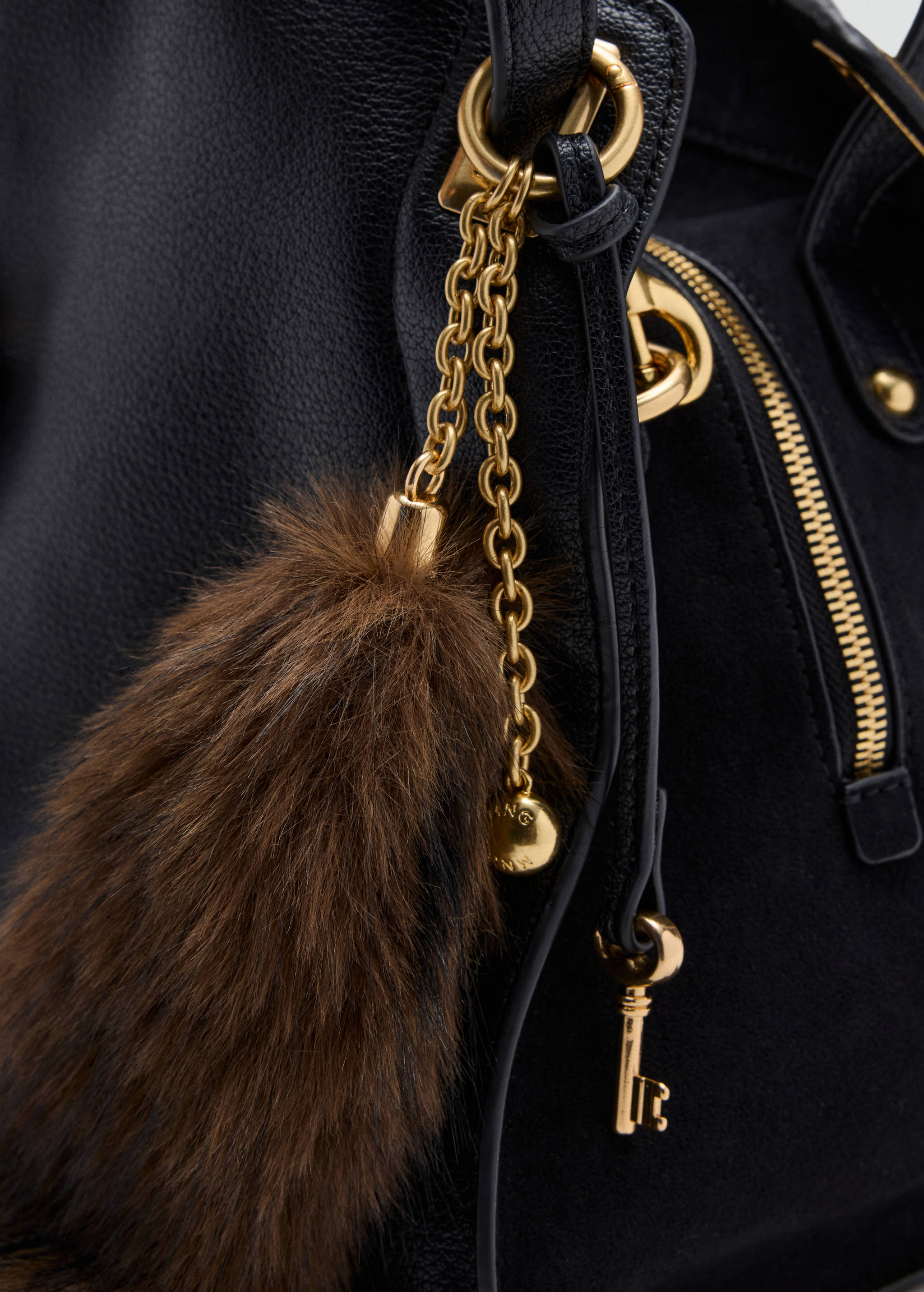 Black shoulder bag detail with a brown faux-fur charm and gold hardware.