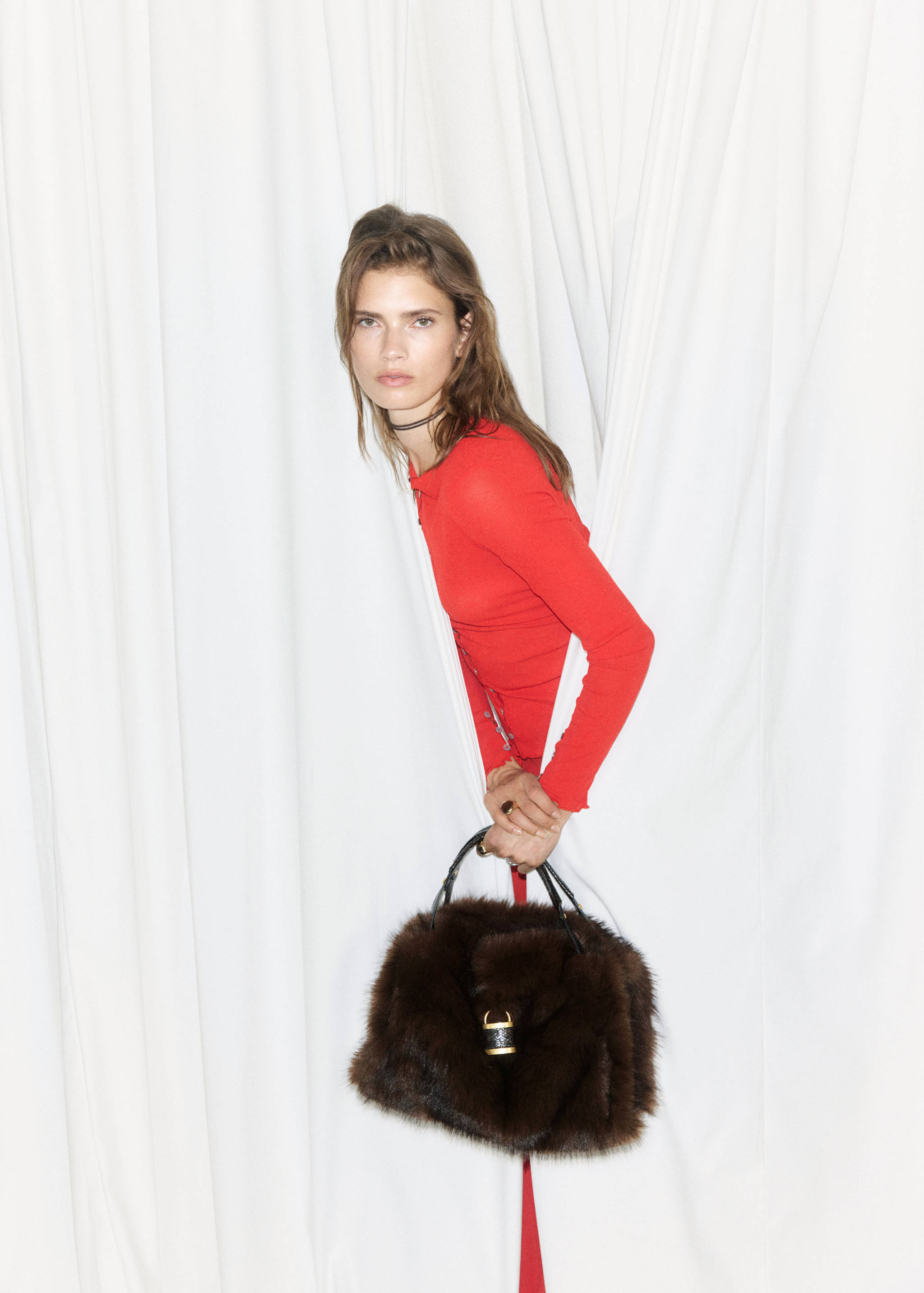 Dark brown faux-fur shoulder bag with a gold clasp, held by a model.