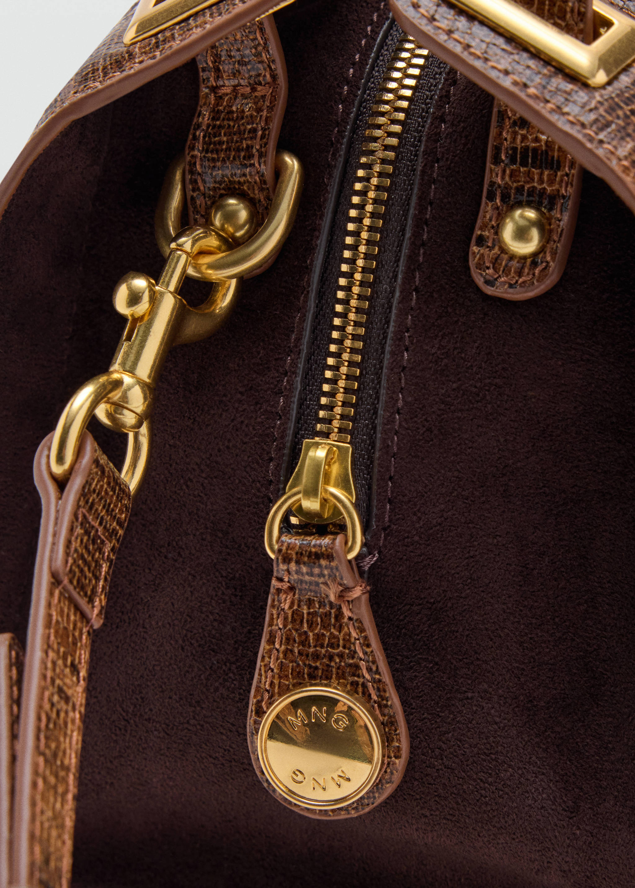 Close-up of a brown suede crossbody bag with gold hardware and embossed trim.