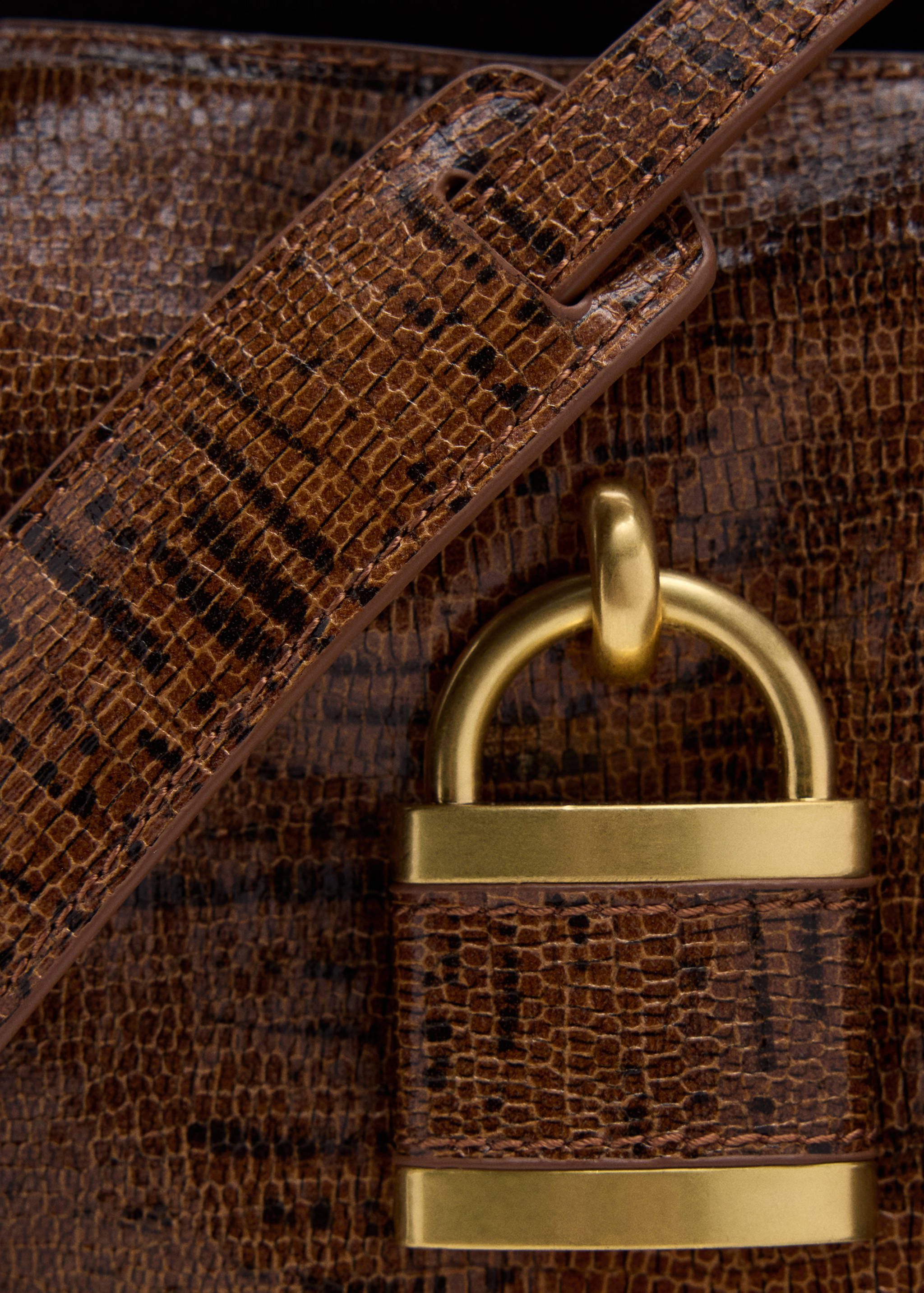 Close-up of a brown embossed crossbody bag featuring a gold padlock detail.