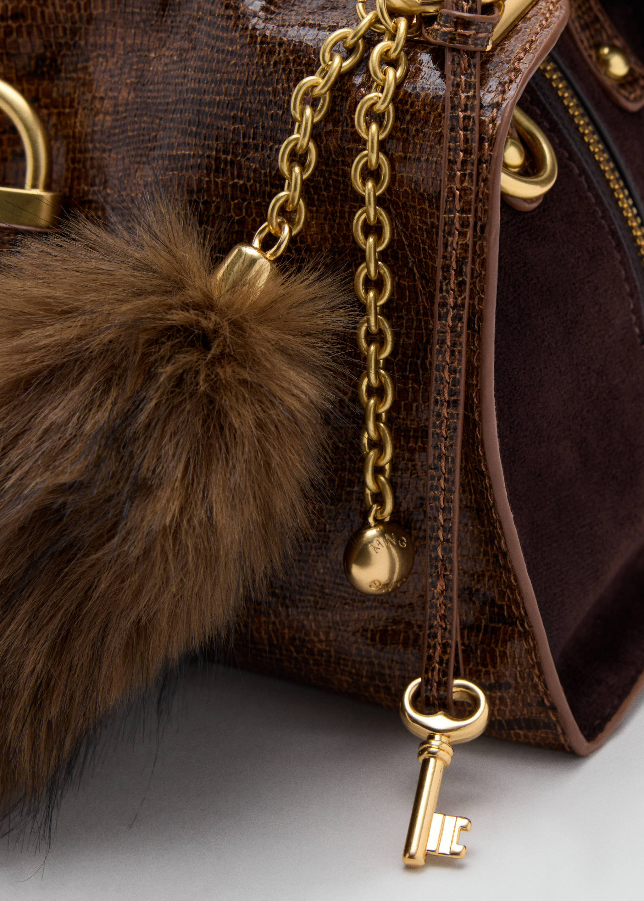 Brown crossbody bag detail with faux-fur pom-pom, key charm and gold hardware.