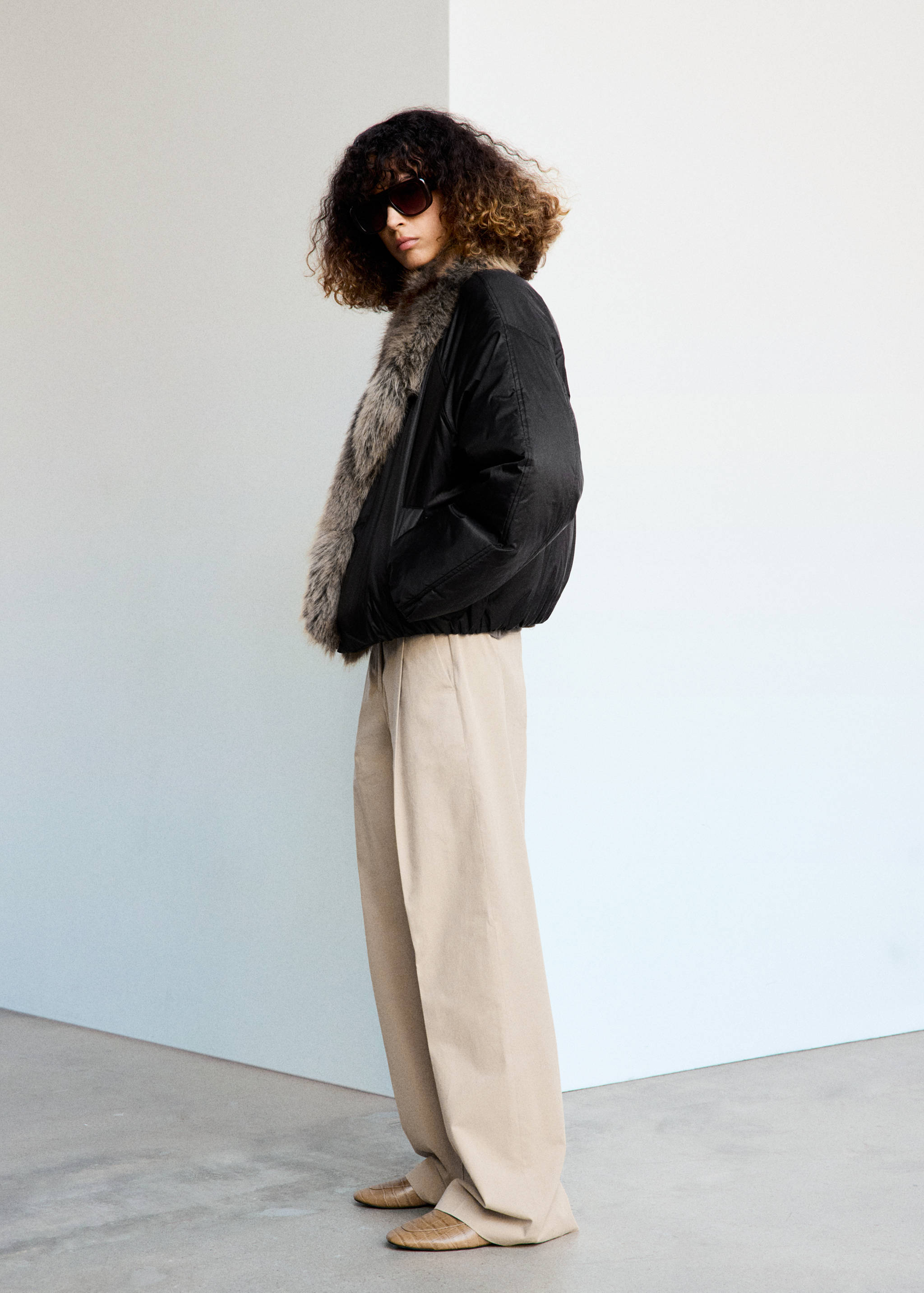 Black anorak with a wide faux-fur collar, worn with beige trousers.