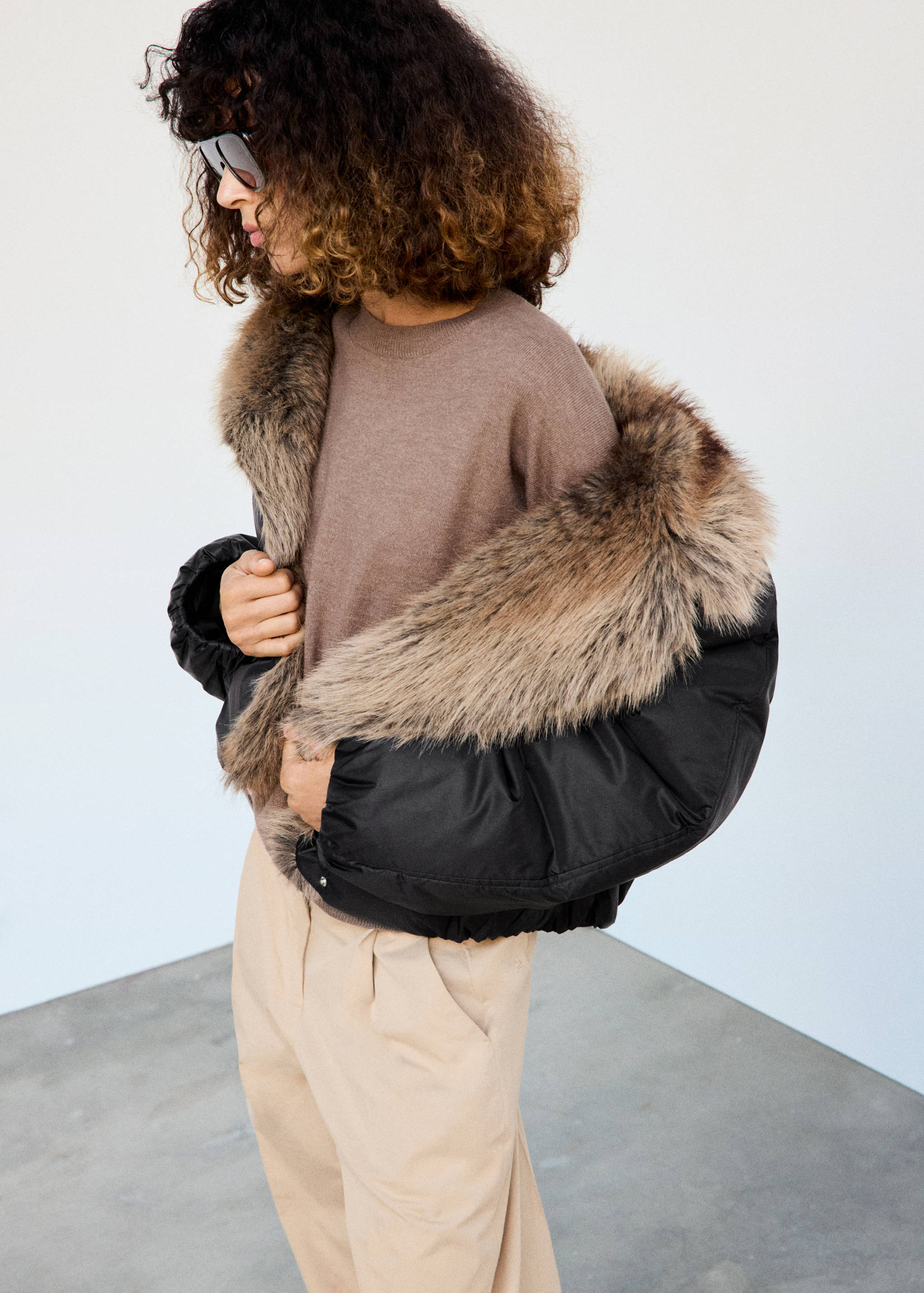 Black anorak with a voluminous faux-fur collar, worn with a knit jumper.