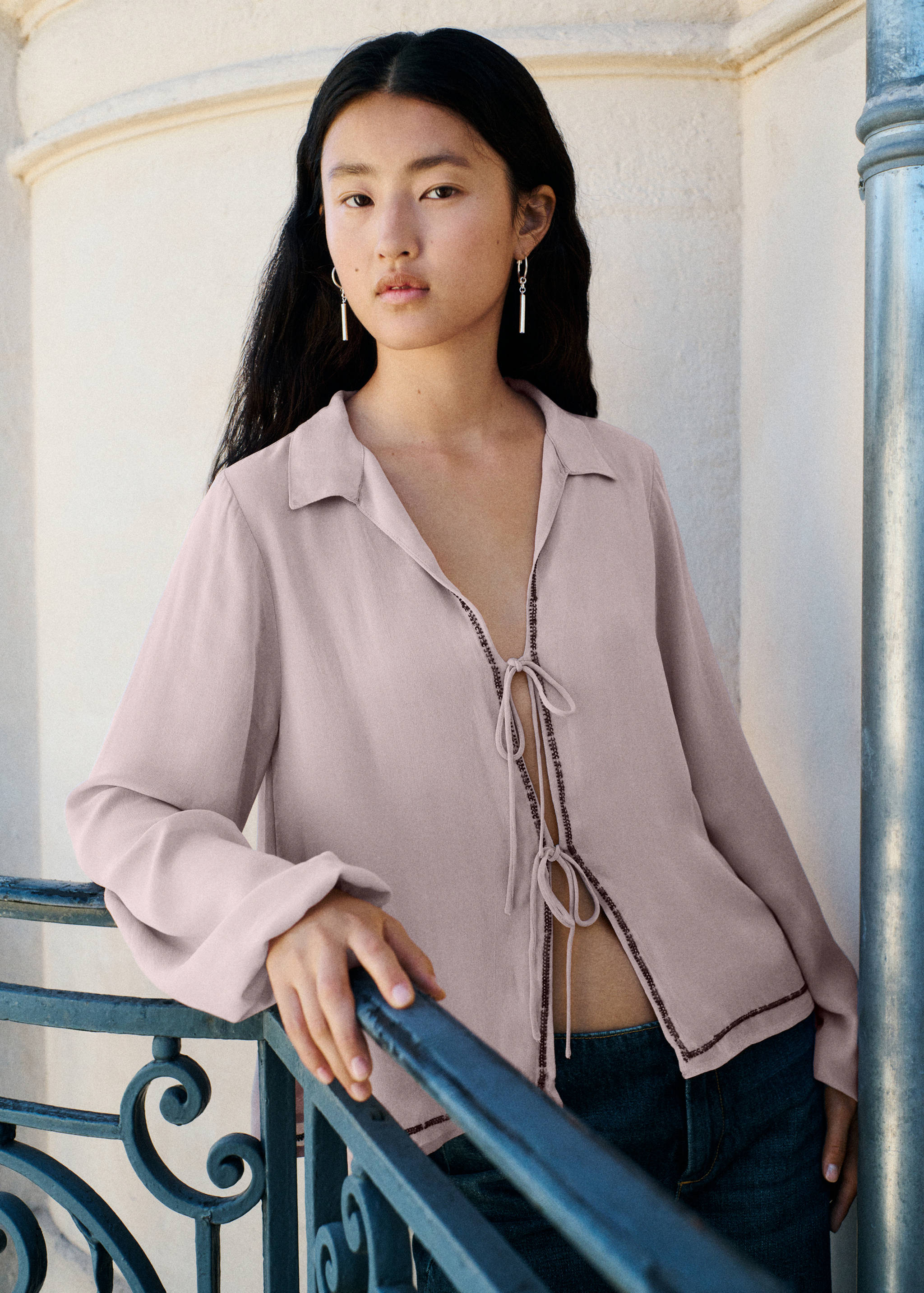 Pale pink tie-front blouse with lapel collar and contrast stitching.