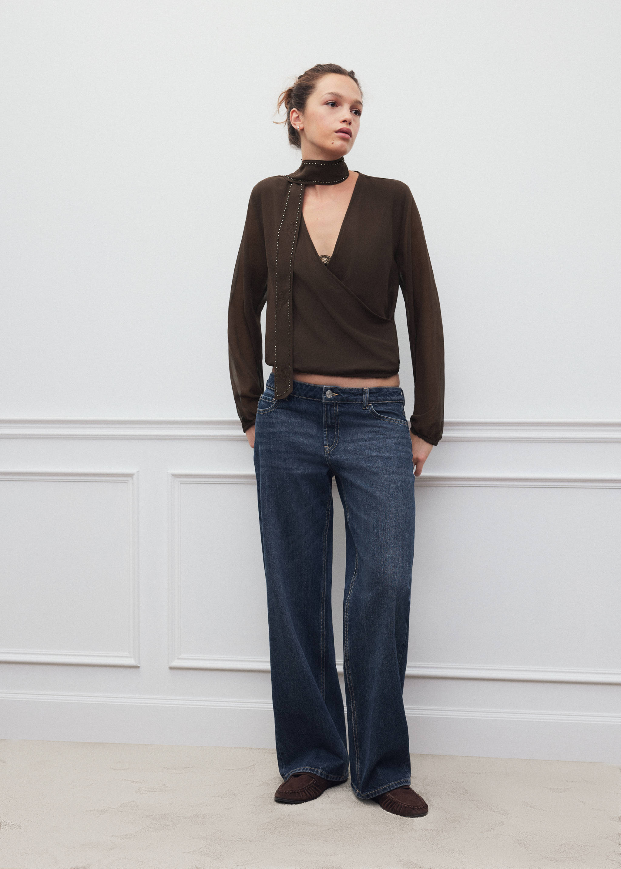 Dark brown wrap shirt with long sleeves and studded choker, worn with blue jeans.