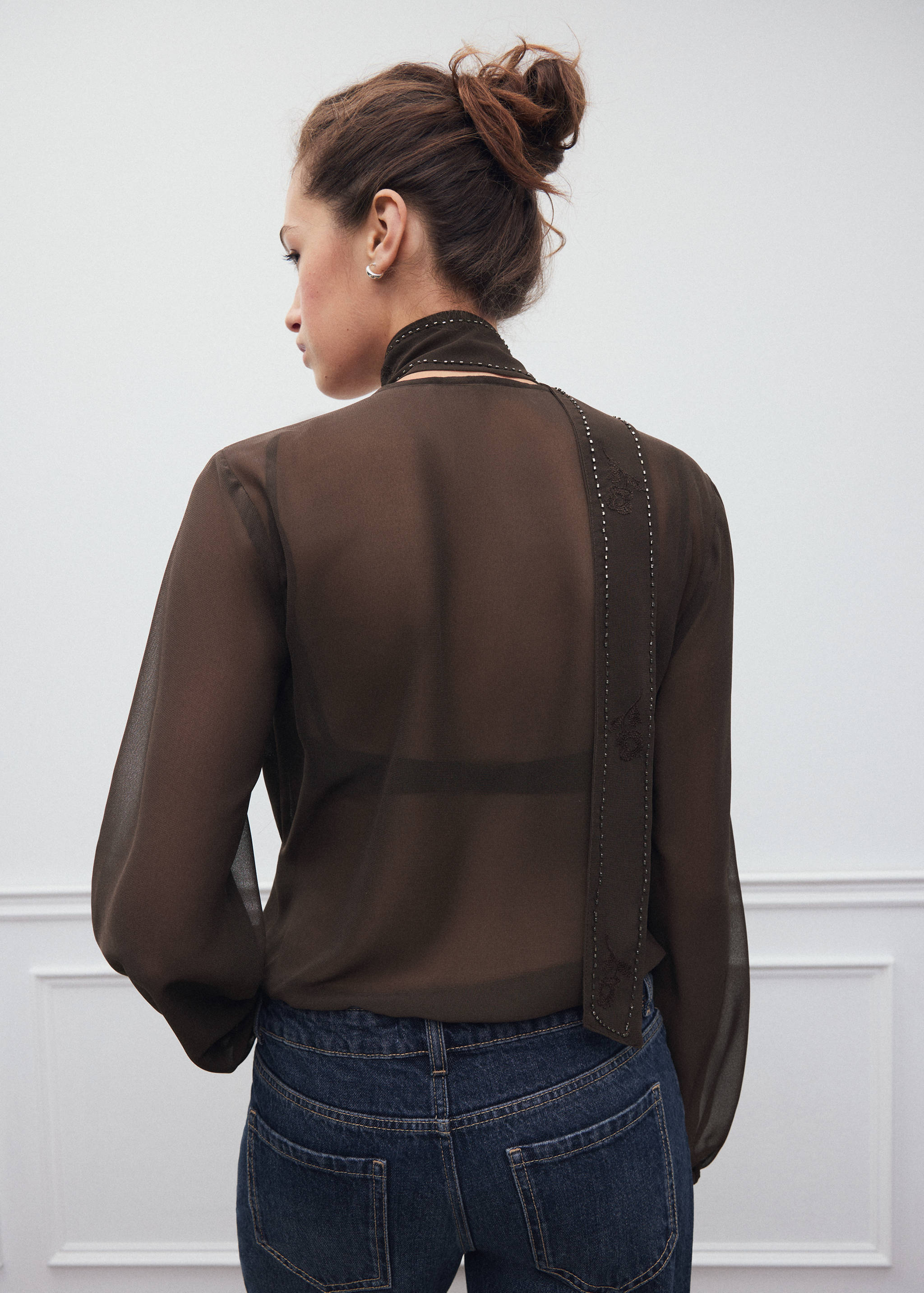 Back view of a dark brown sheer shirt with a high neck and studded scarf detail.