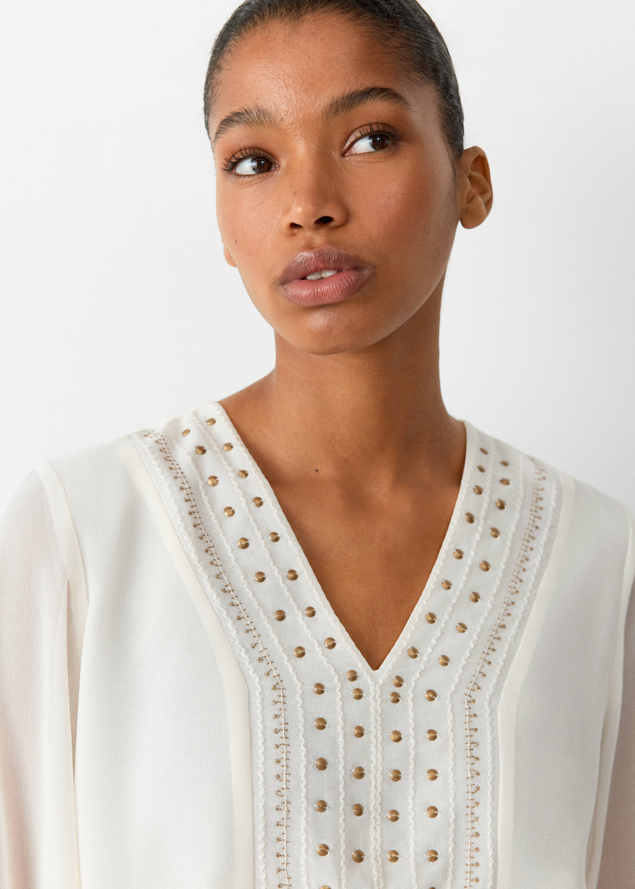 White shirt with a V-neckline, gold-toned studs, and embroidered trim.