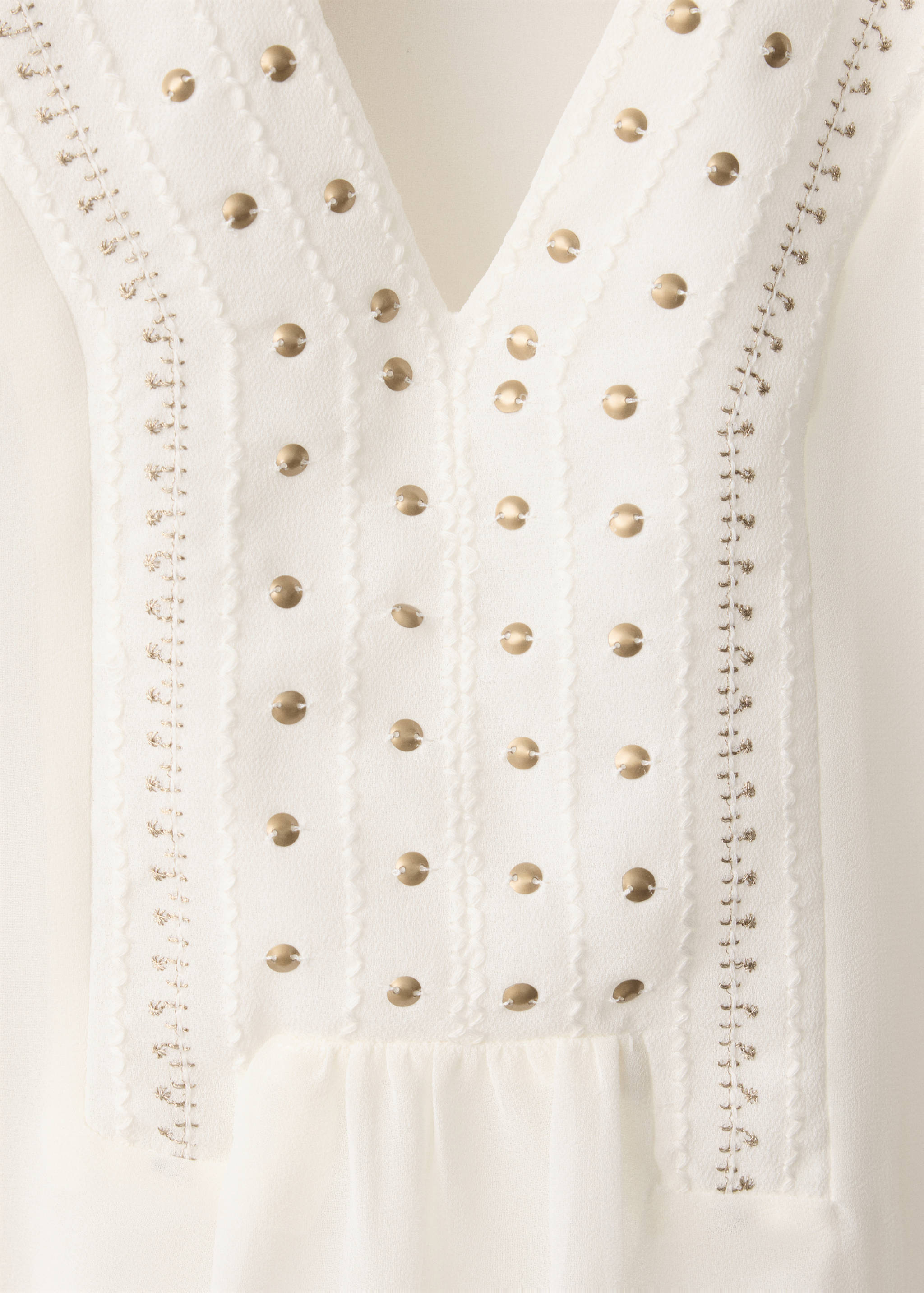 White shirt with a V-neck and metallic gold stud details.