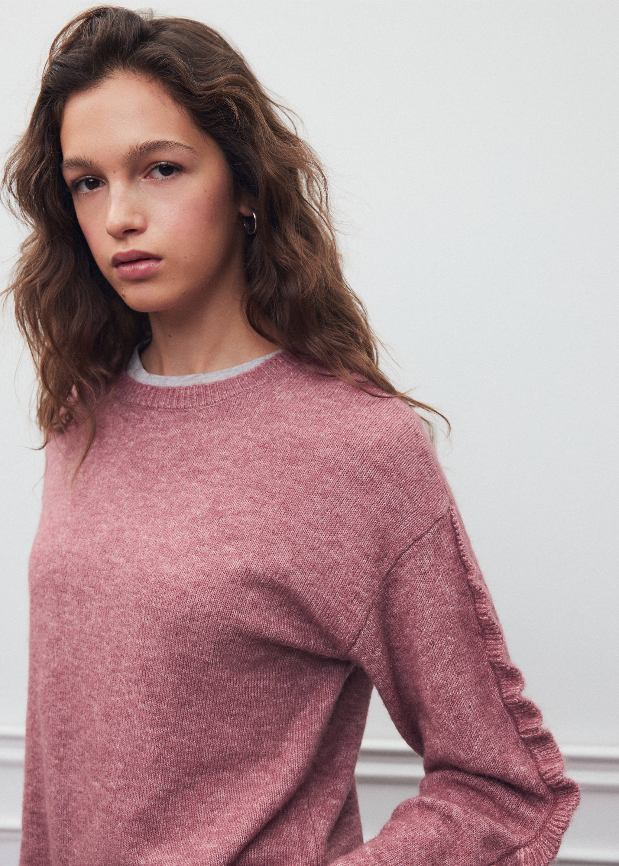 Pink knitted jersey with ruffled shoulder seams, crew neck and model's face.
