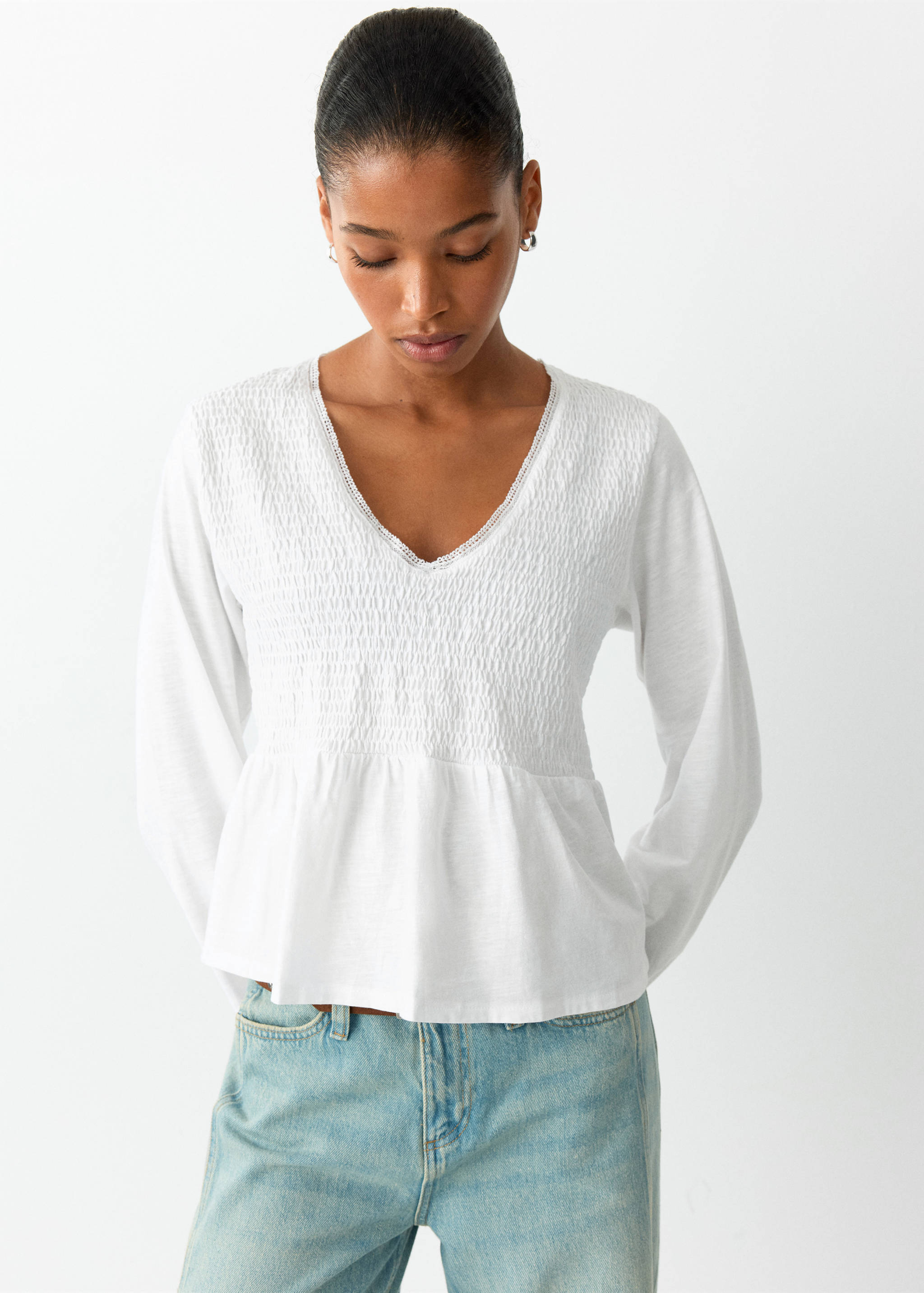 White long-sleeved t-shirt with a smocked bodice, lace-trimmed V-neck, and peplum hem.
