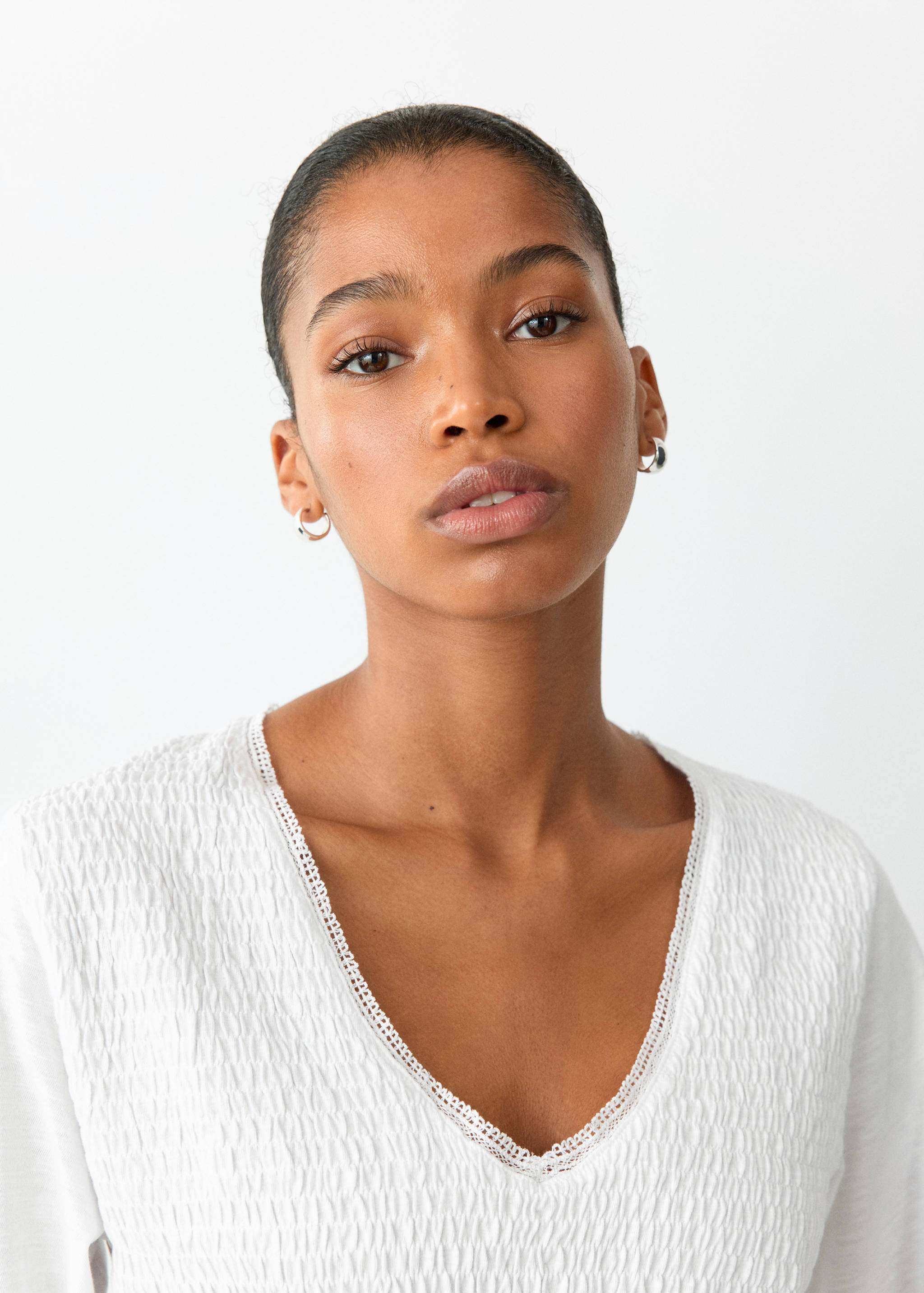 White t-shirt with a smocked texture and V-neckline trimmed with lace, shown in a close-up portrait.