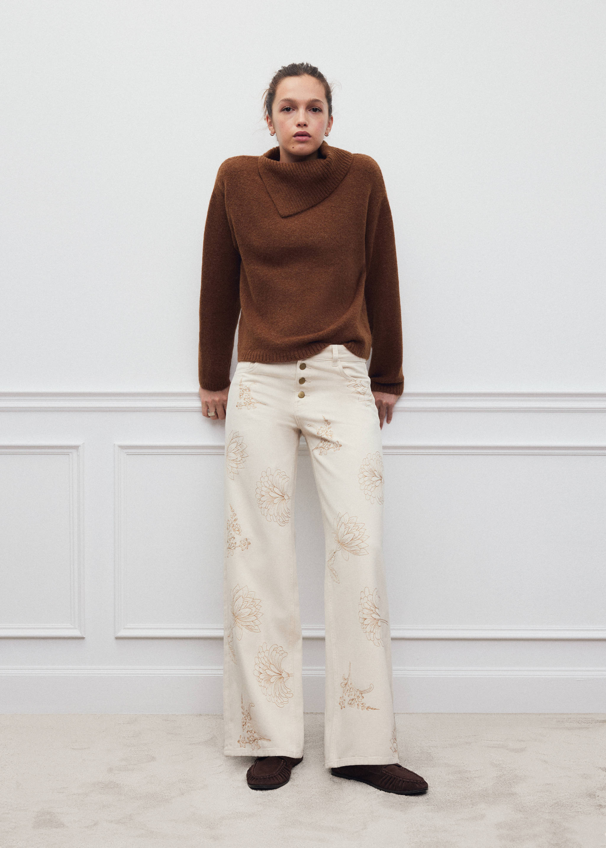 Brown jersey with an asymmetrical cowl neck, worn with embroidered cream trousers.