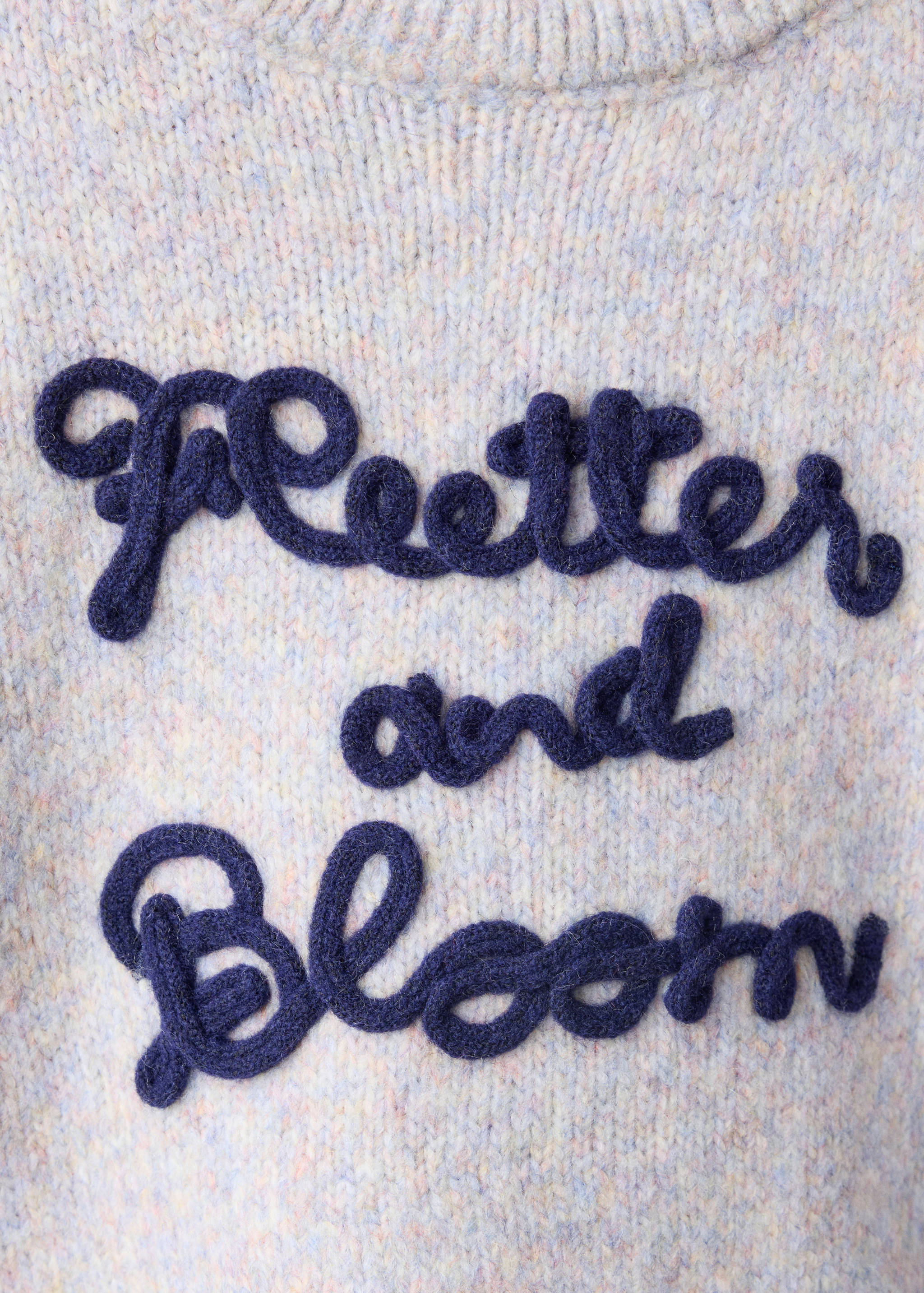 Close-up of a pastel multicoloured knit sweater with raised navy embroidered lettering.