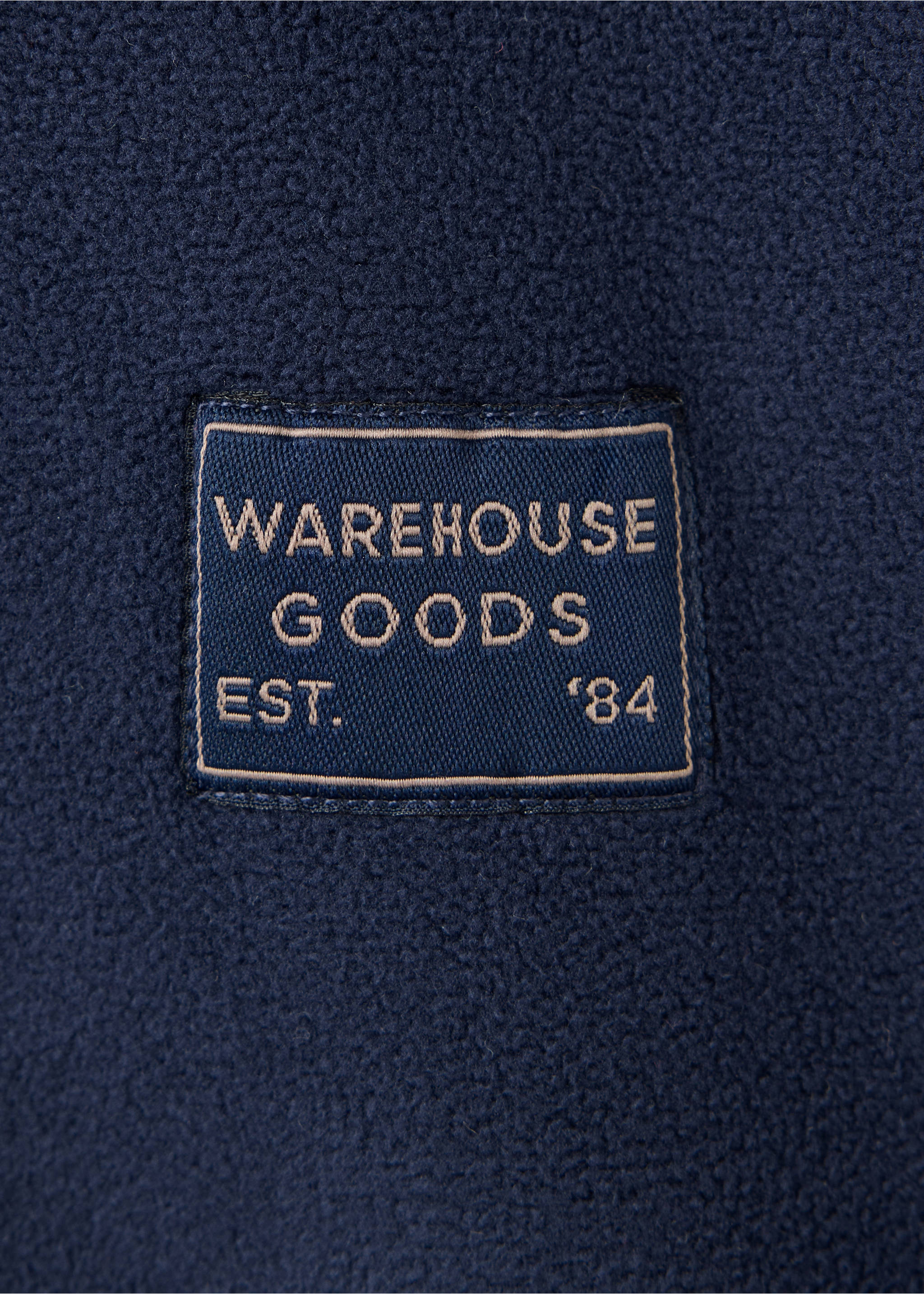 Navy fleece sweatshirt detail with a WAREHOUSE GOODS embroidered patch., Navy. Ref: 37008636-00.