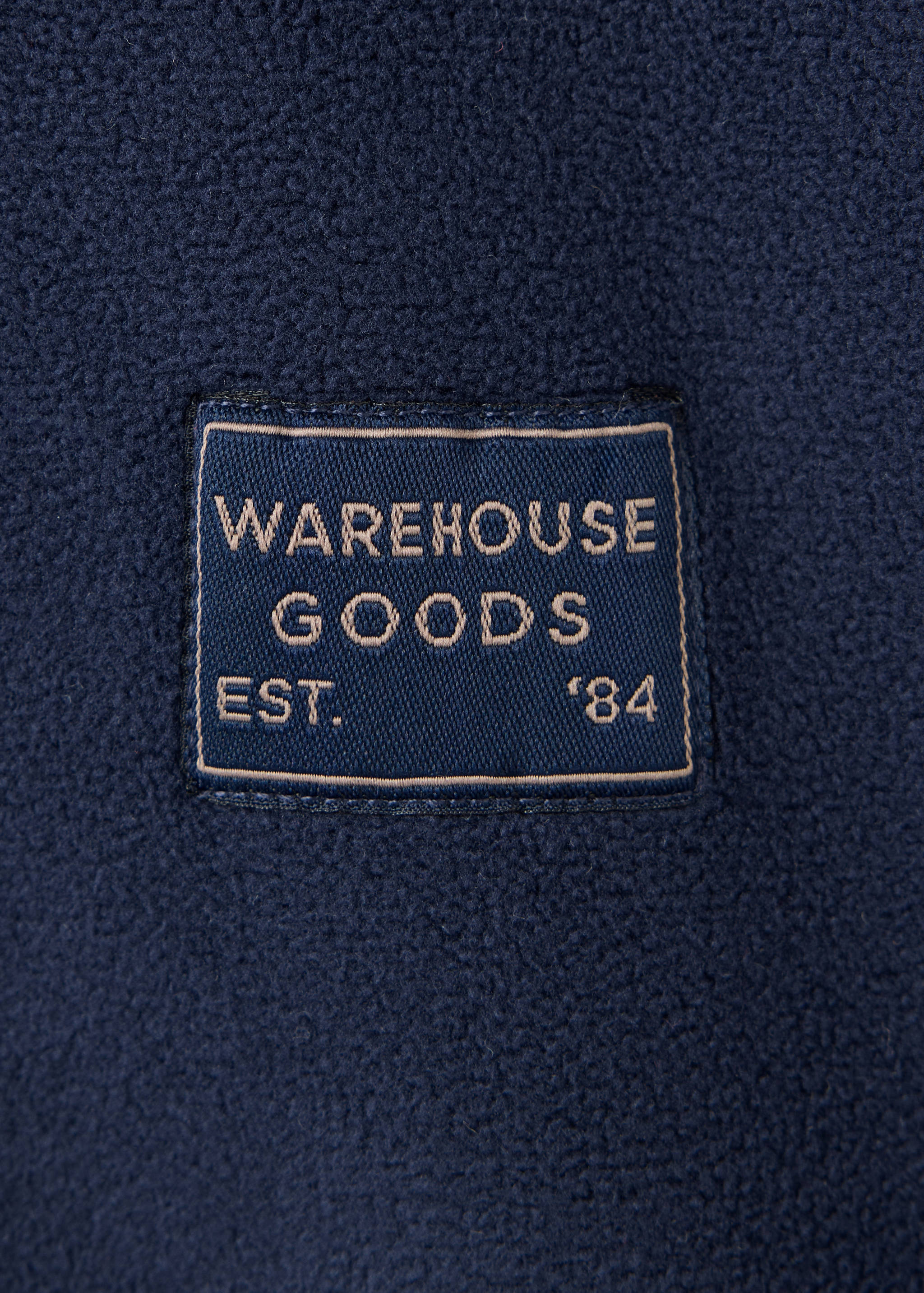 Navy fleece sweatshirt detail with a WAREHOUSE GOODS embroidered patch.