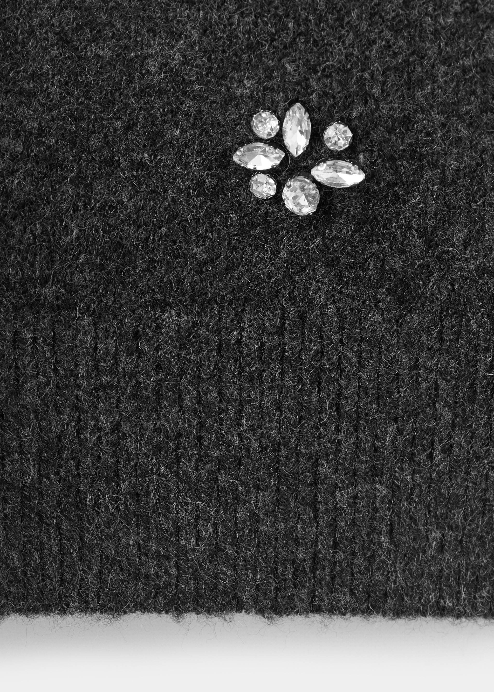 Dark grey jersey fabric detail showing a fuzzy knit texture, ribbed hem, and a cluster of rhinestones.