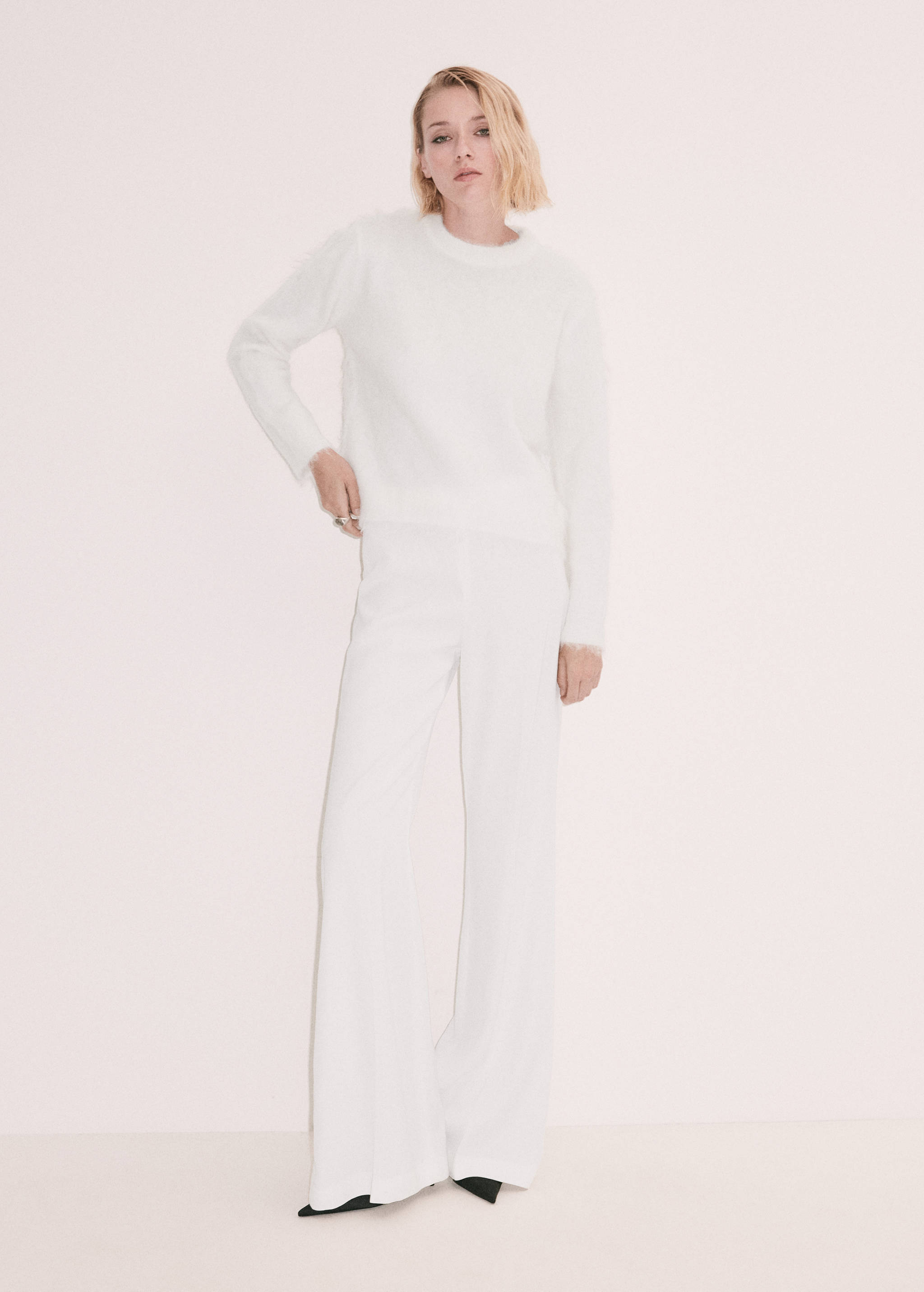 White fluffy knit jersey with round neck and long sleeves, worn with trousers.