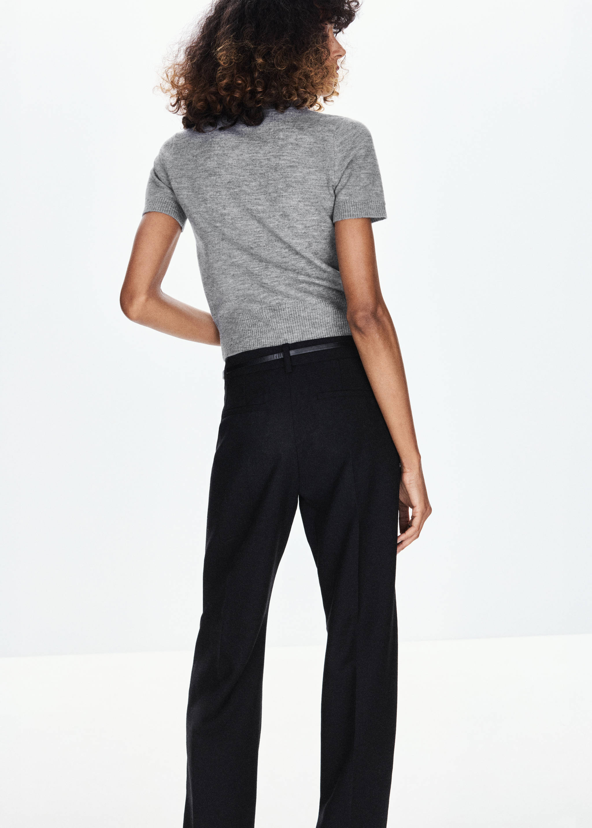 Grey short-sleeved knitted jersey shown from the back, paired with black trousers.