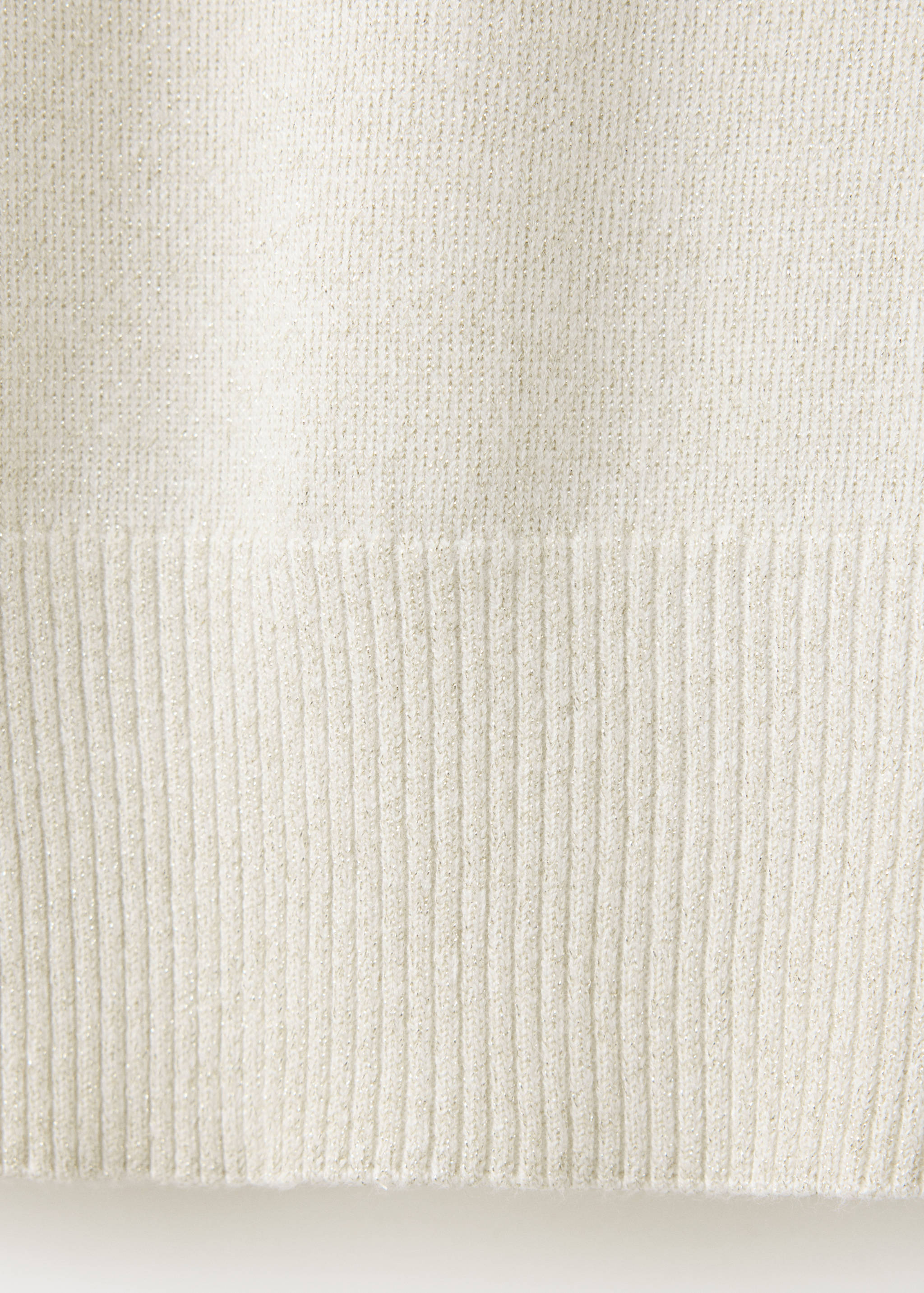 Close-up of an off-white jumper fabric showing a fine knit with metallic threads and a ribbed hem.