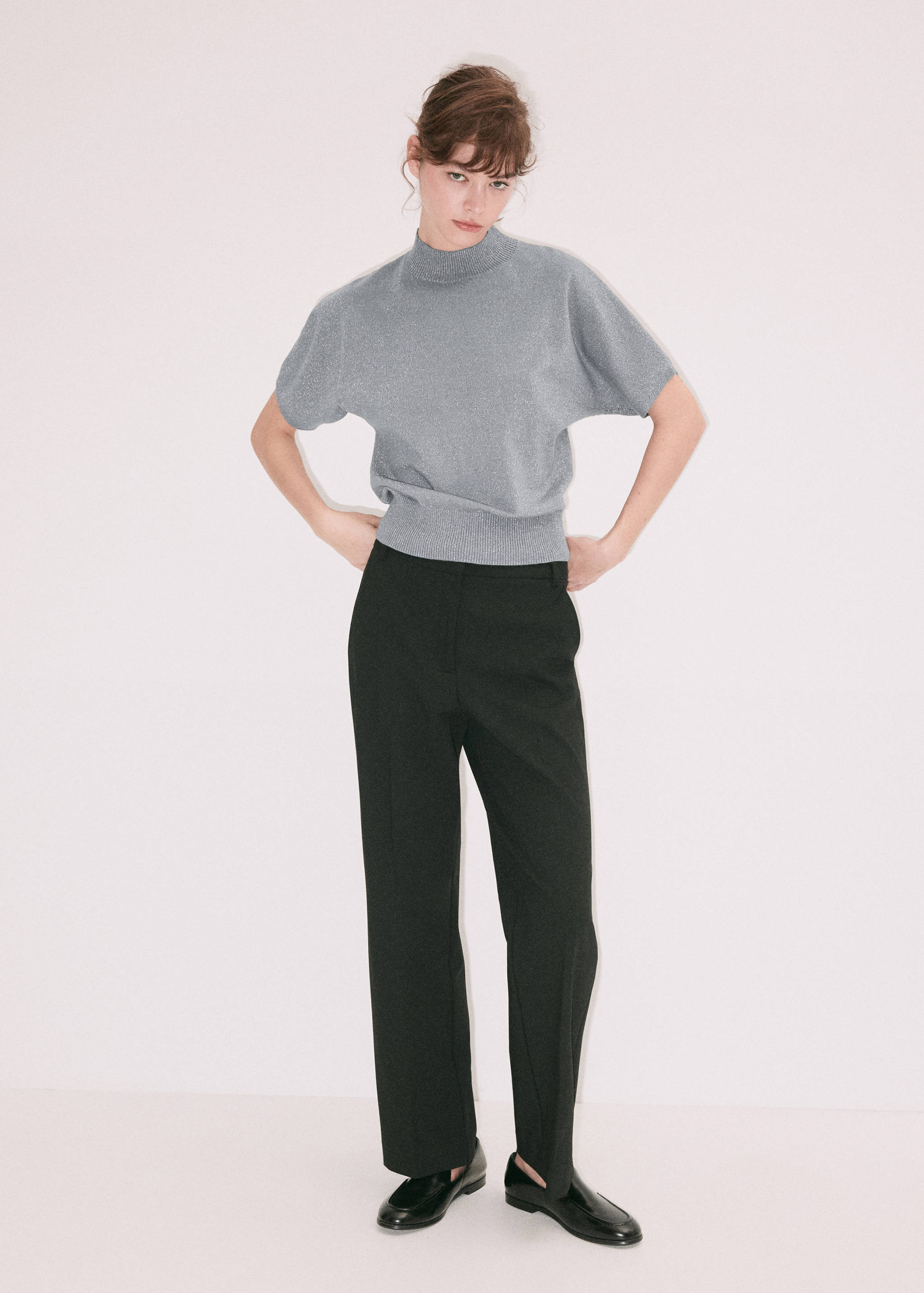 Grey metallic short-sleeve jersey with a high neck, worn with black trousers.