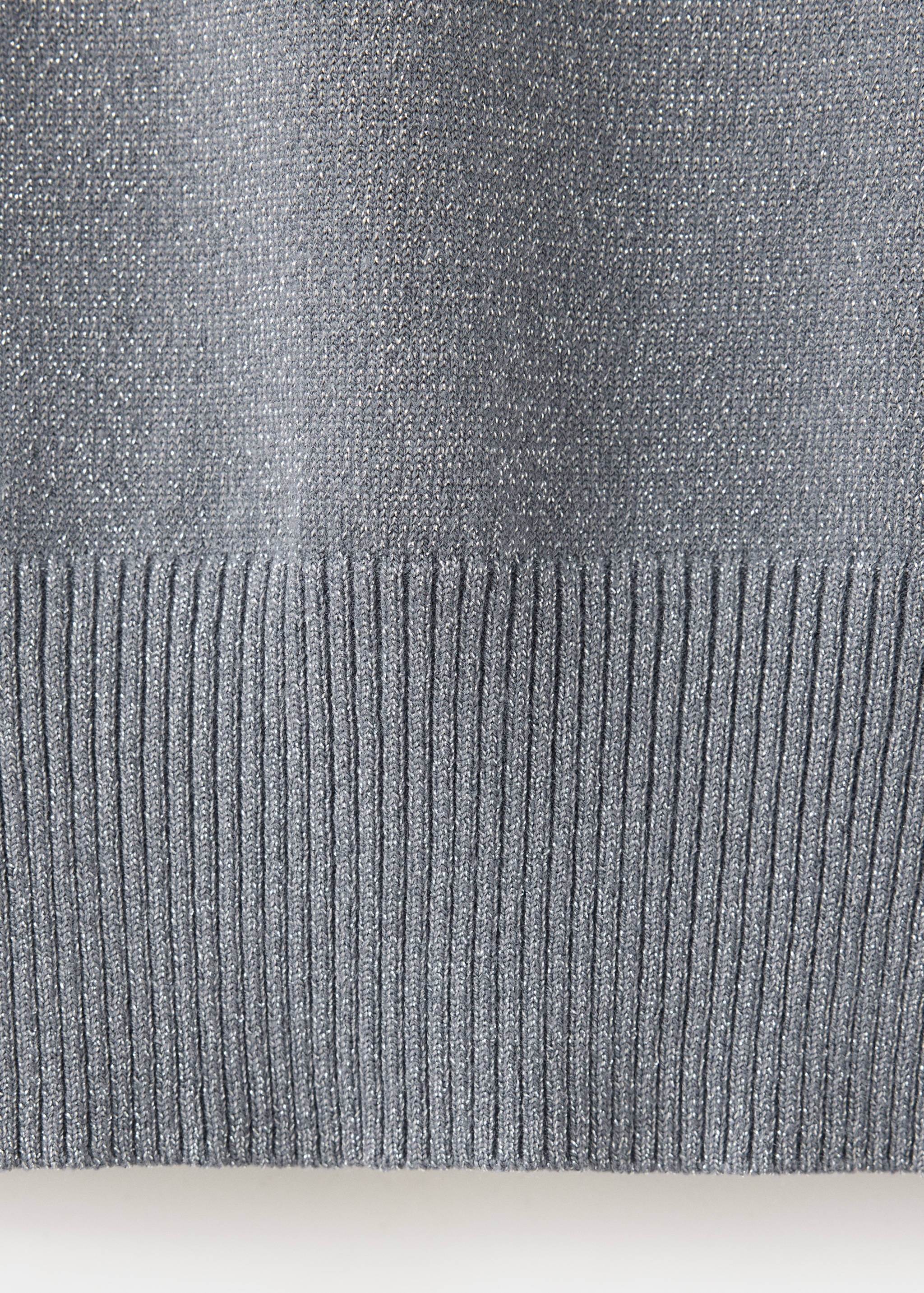 Close-up of a grey metallic-thread knitted jumper with a ribbed hem.