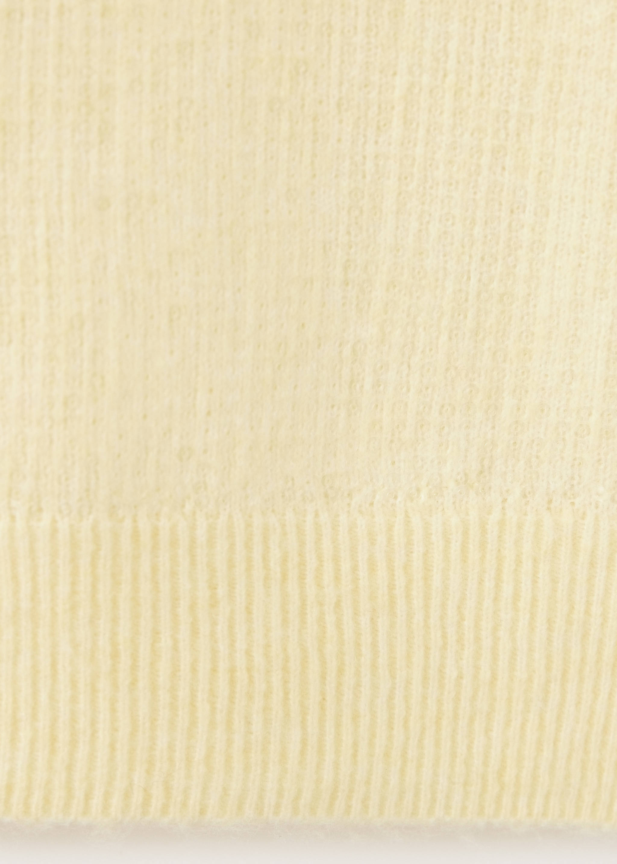 Primer plano de un tejido de punto fino de color amarillo pálido con textura y dobladillo de canalé.