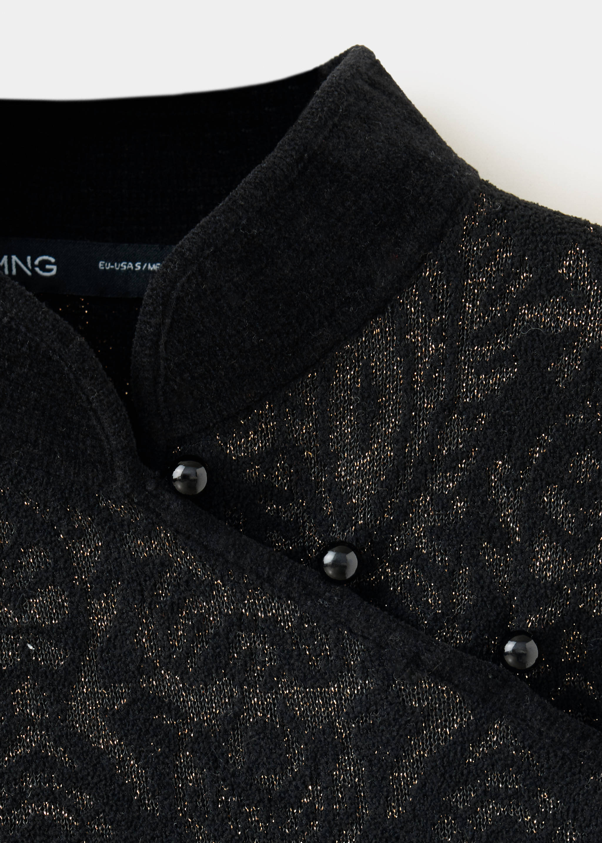 Detalle de jersey negro de jacquard con cuello mao y tira de botones asimétrica.