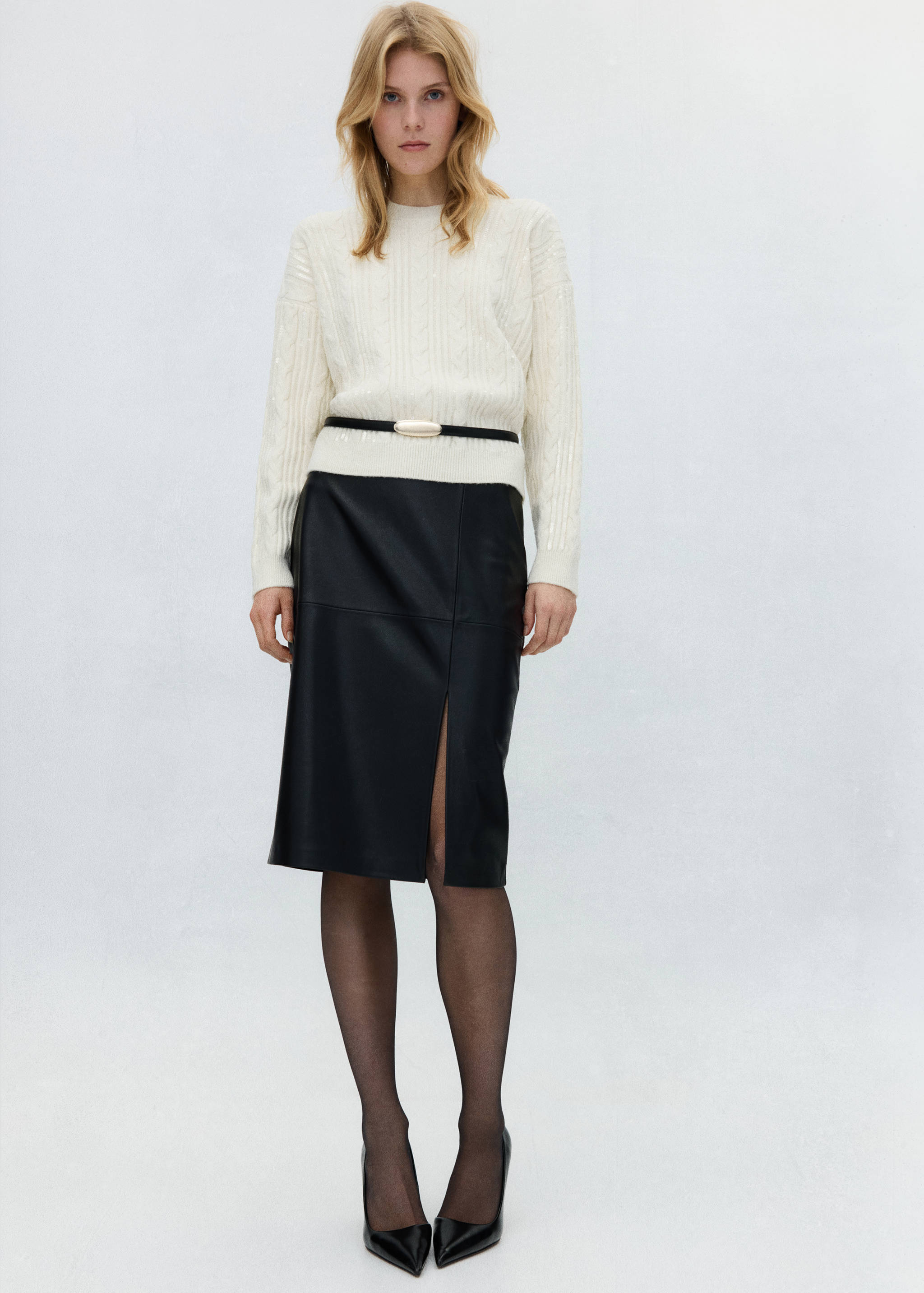 Cream cable-knit jumper worn with a black faux-leather midi skirt and thin belt.